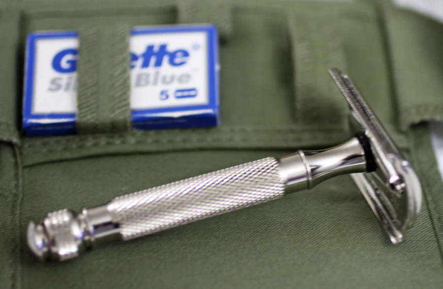 A chrome safety razor and gillette blades on green fabric.