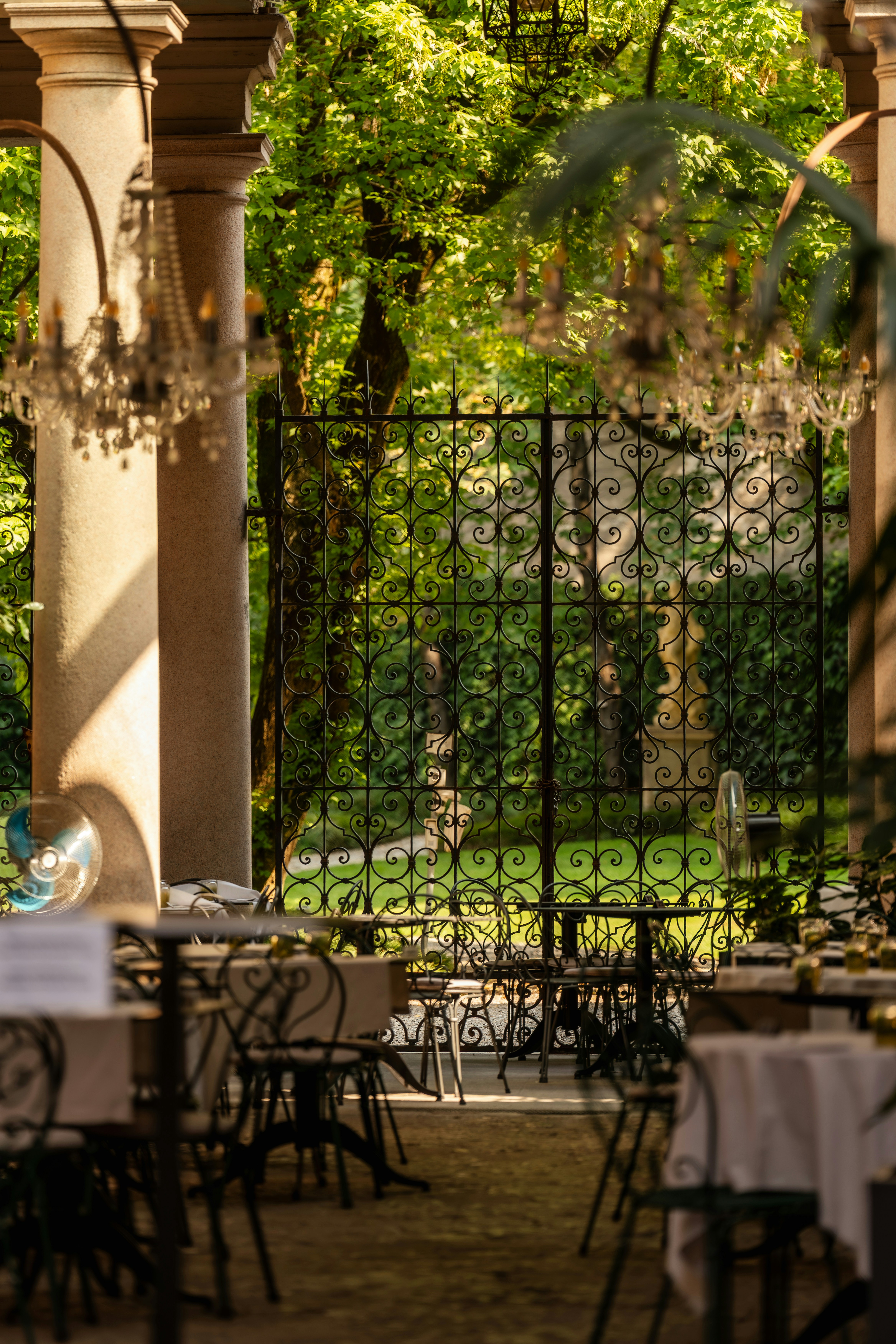 Comedor exterior ornamentado con candelabros y un jardín exuberante.