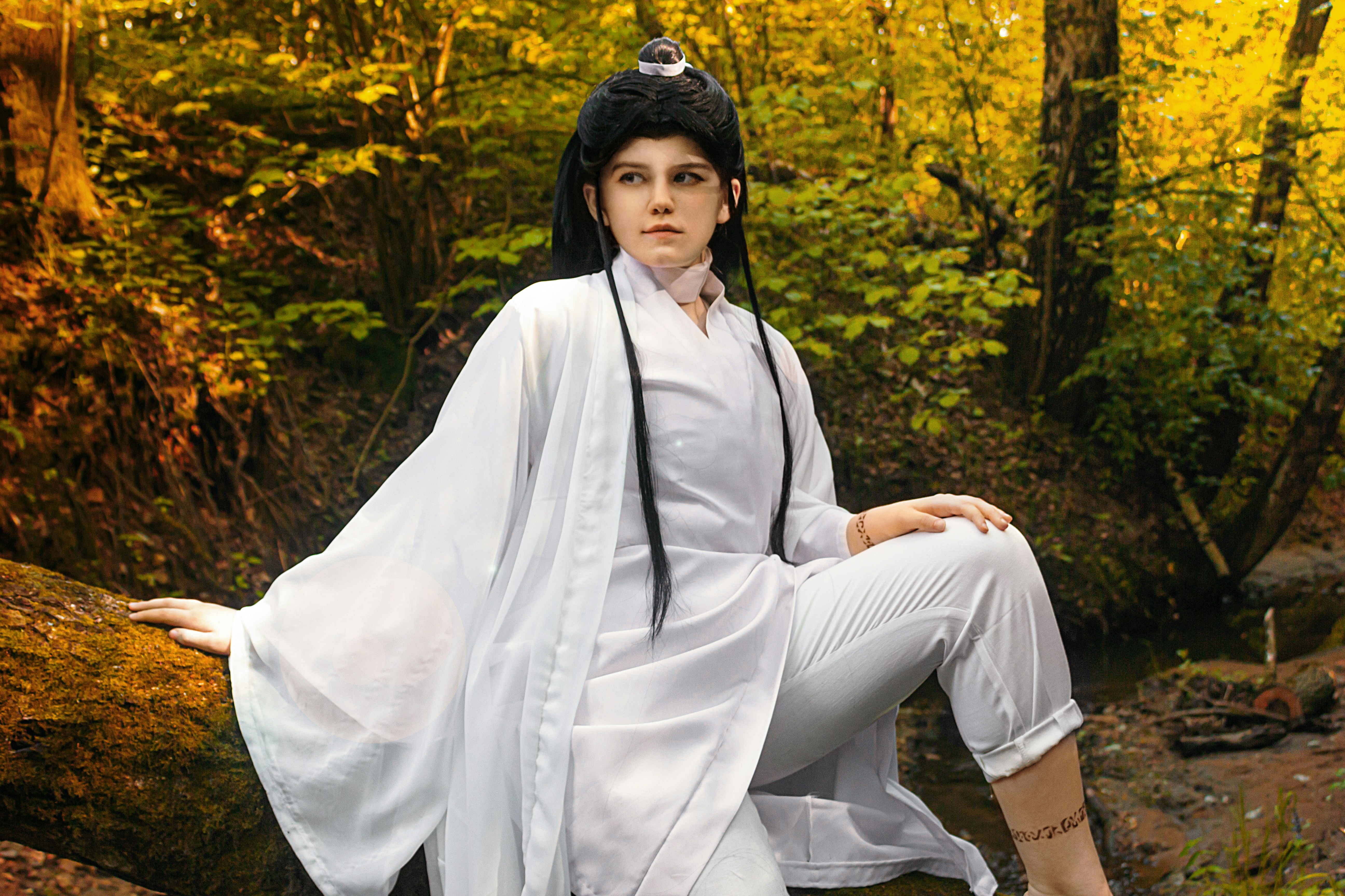 Une femme en robes traditionnelles blanches est assise sur une bûche de forêt.