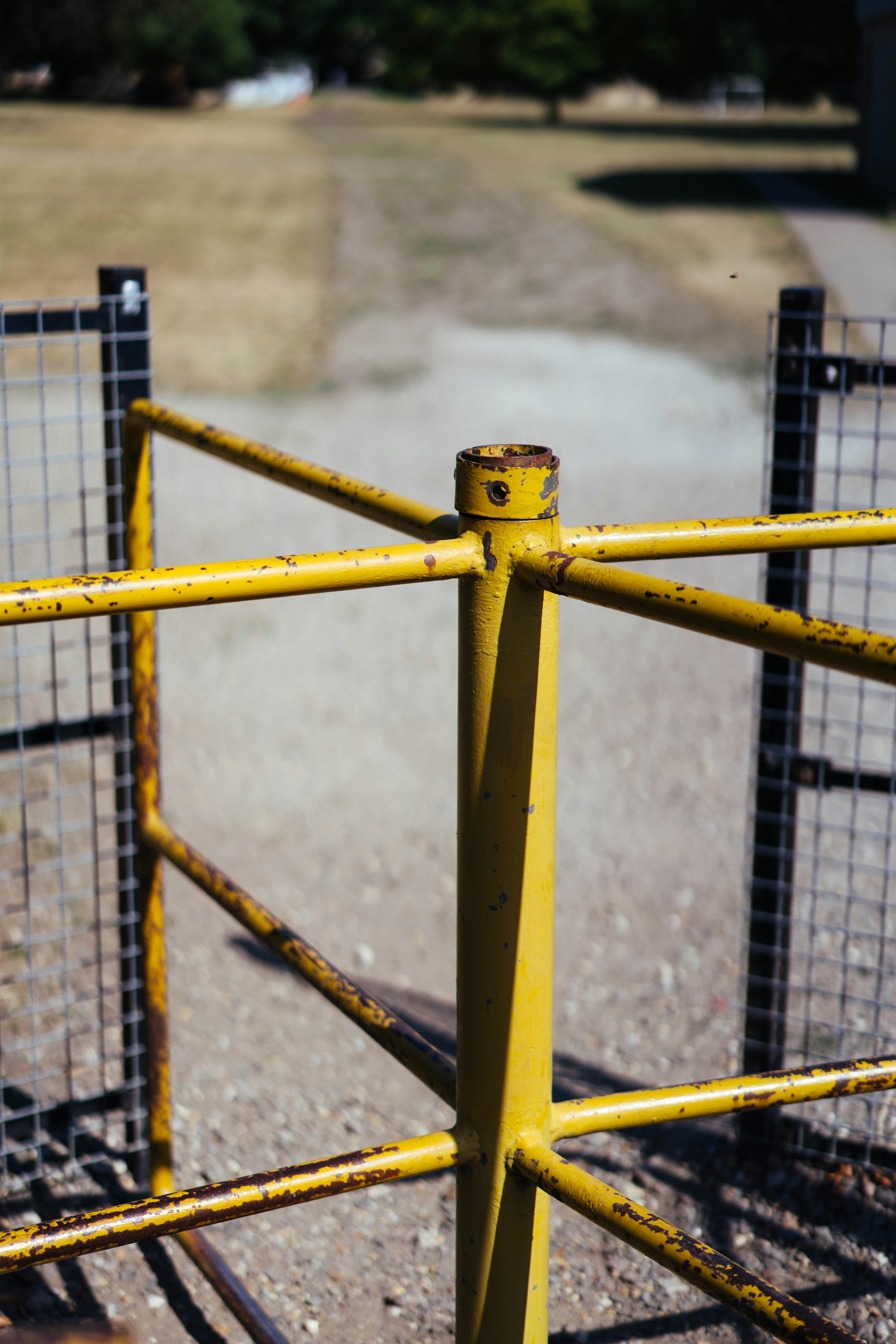A rusty yellow metal gate stands on a dirt path.
