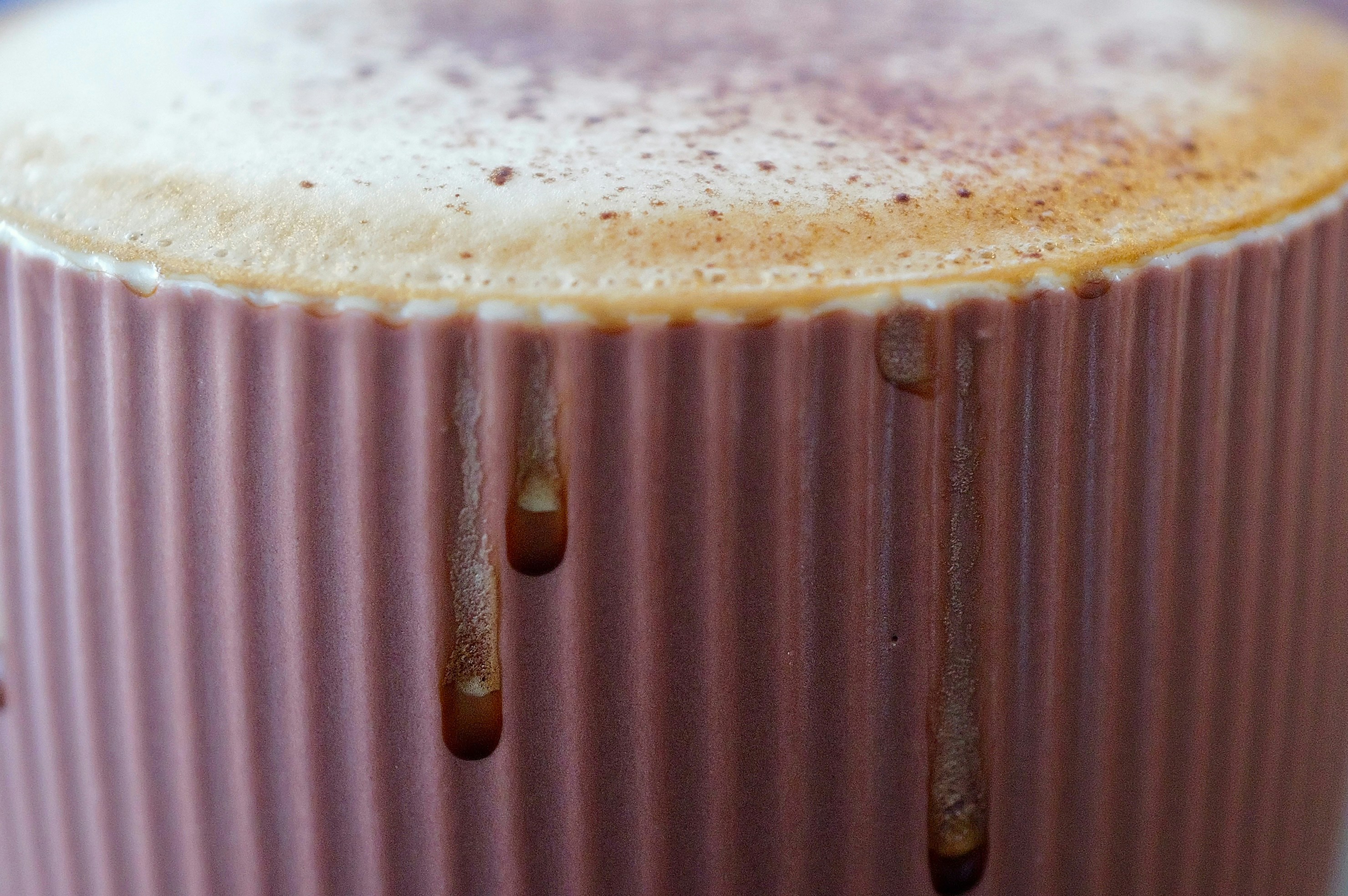 Frothy drink in a pink ribbed mug with drips