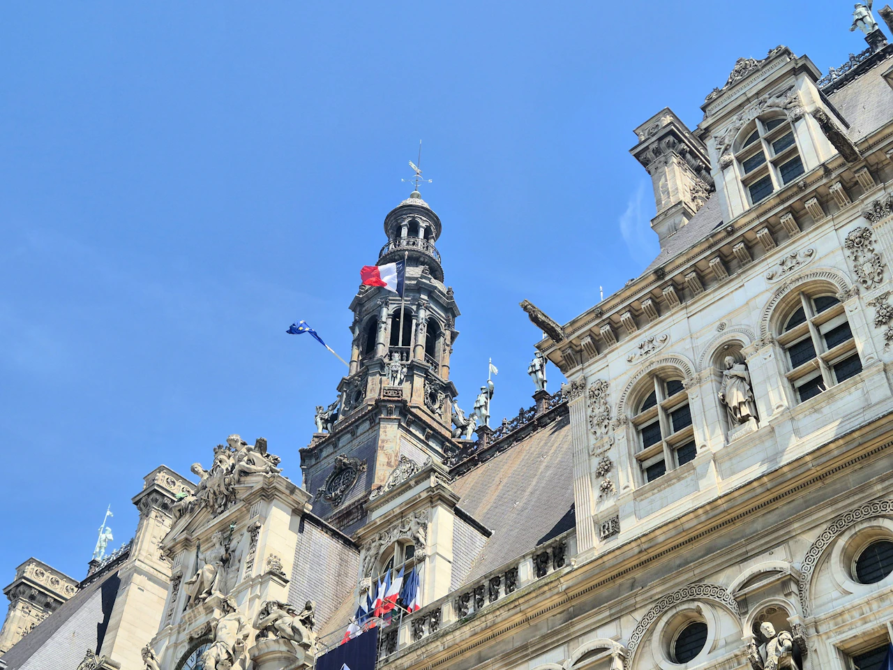 Ornate historic French government building with a clock tower and tricolour flags