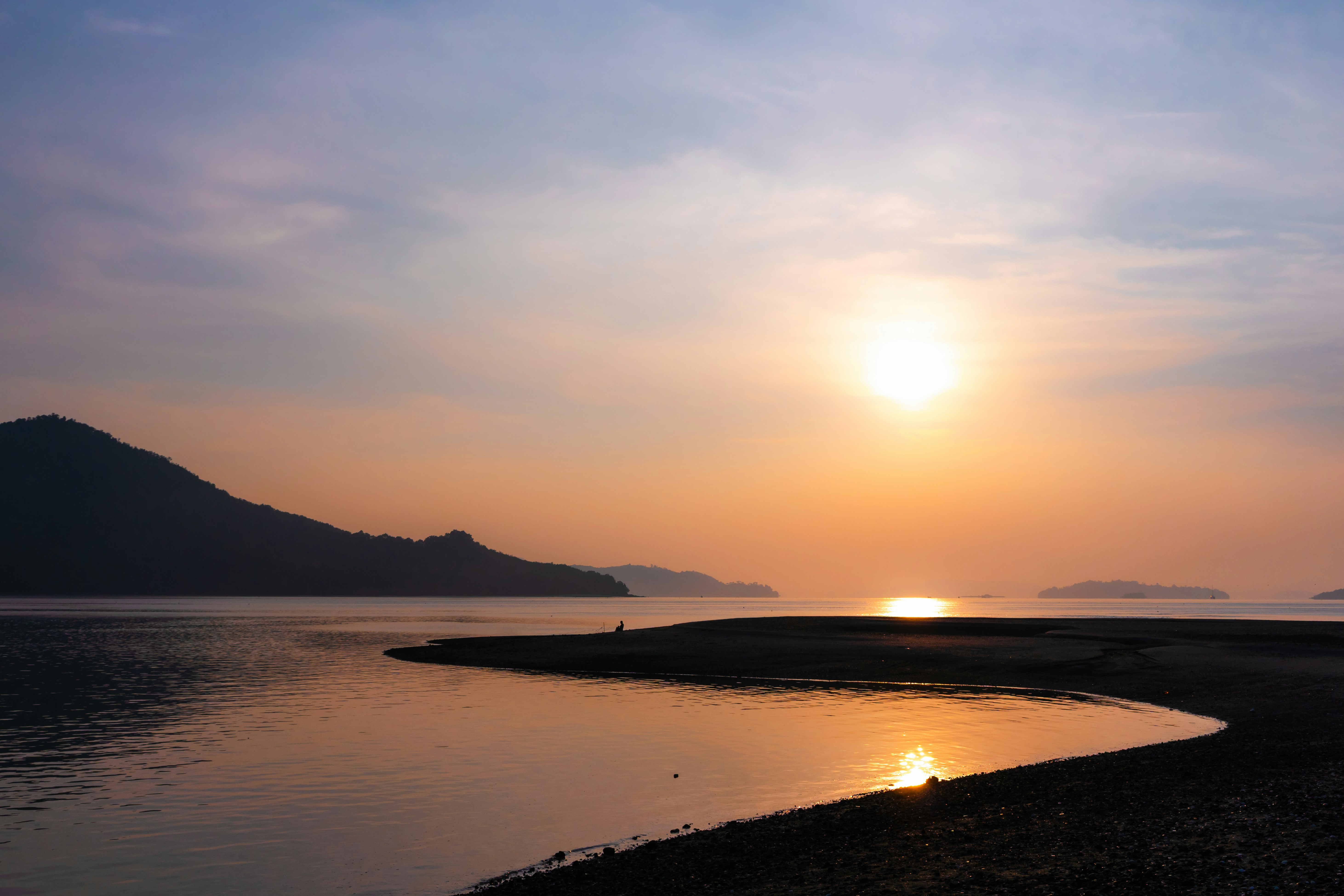 Coucher de soleil doré sur une eau calme avec des montagnes et un rivage lointains.