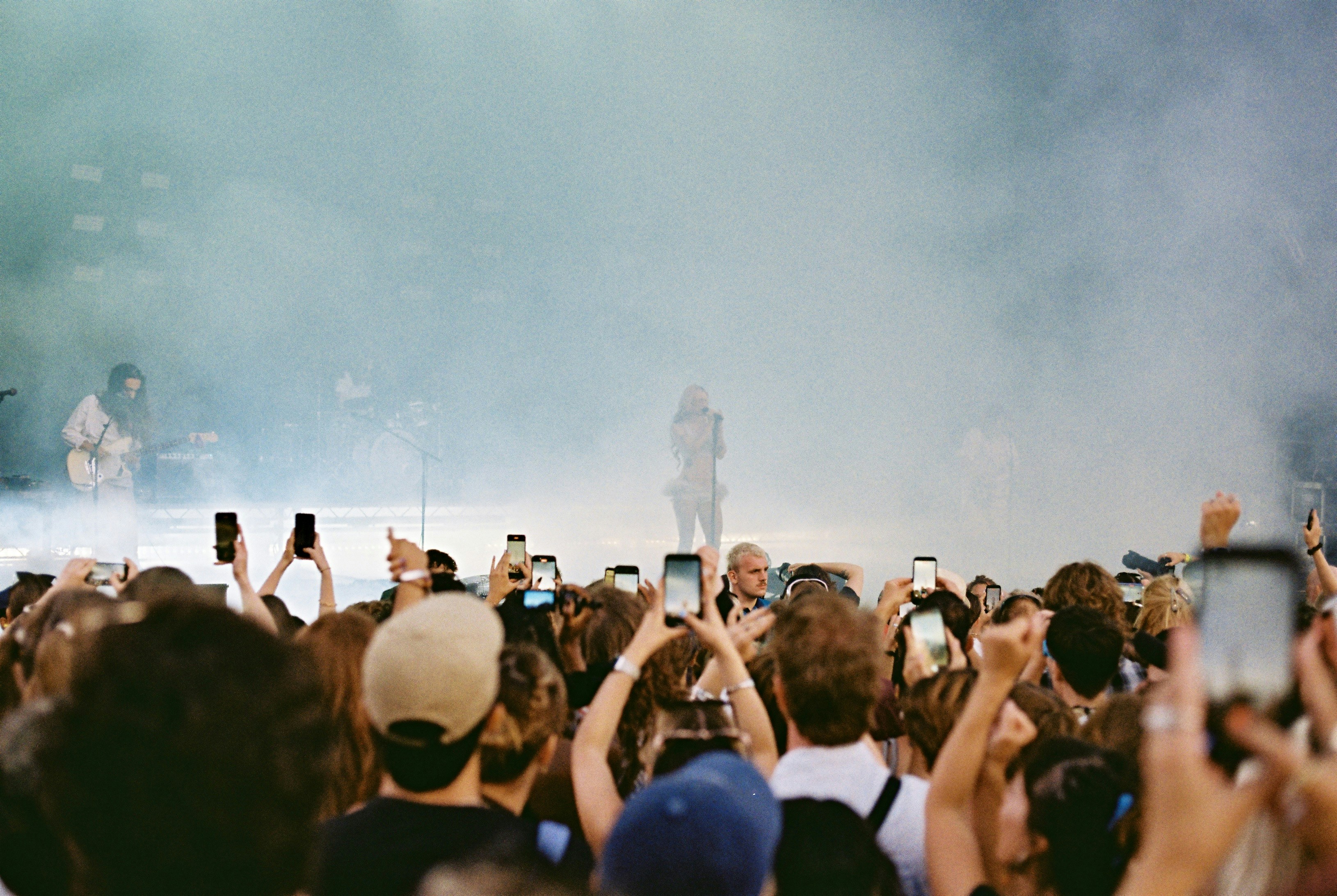 Raised phones frame distant performers through soft festival smoke