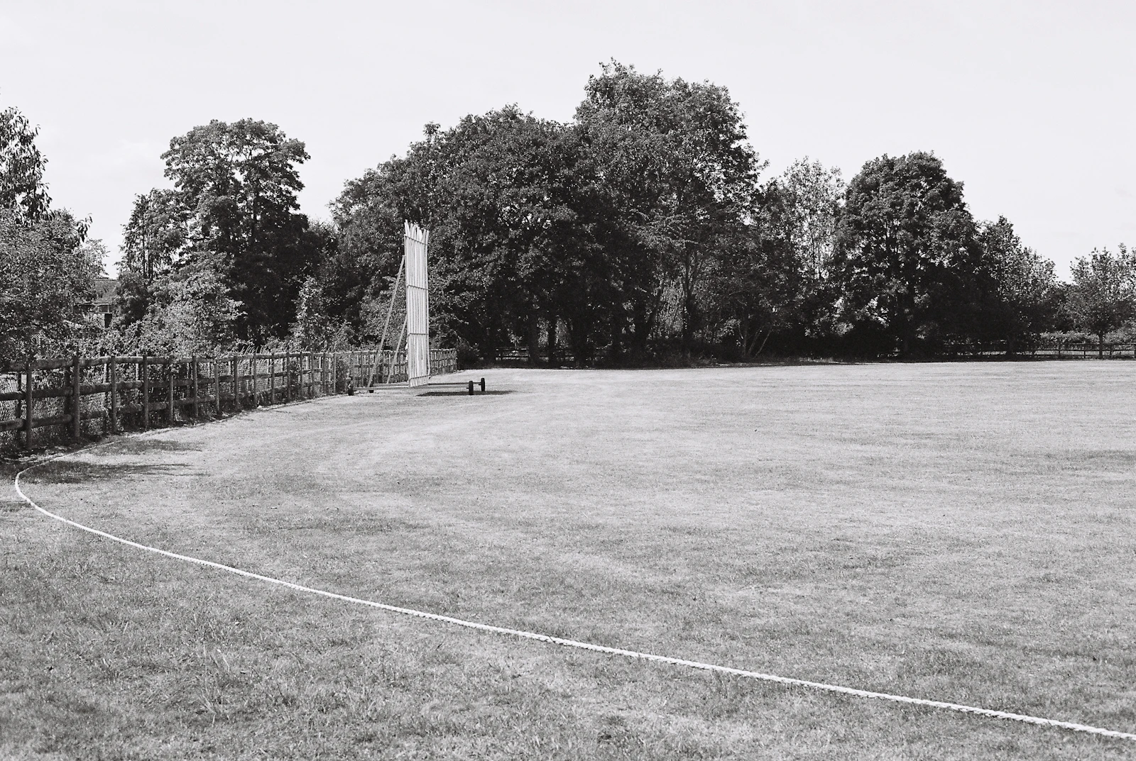 A village cricket ground with a sightscreen at the boundary and trees behind