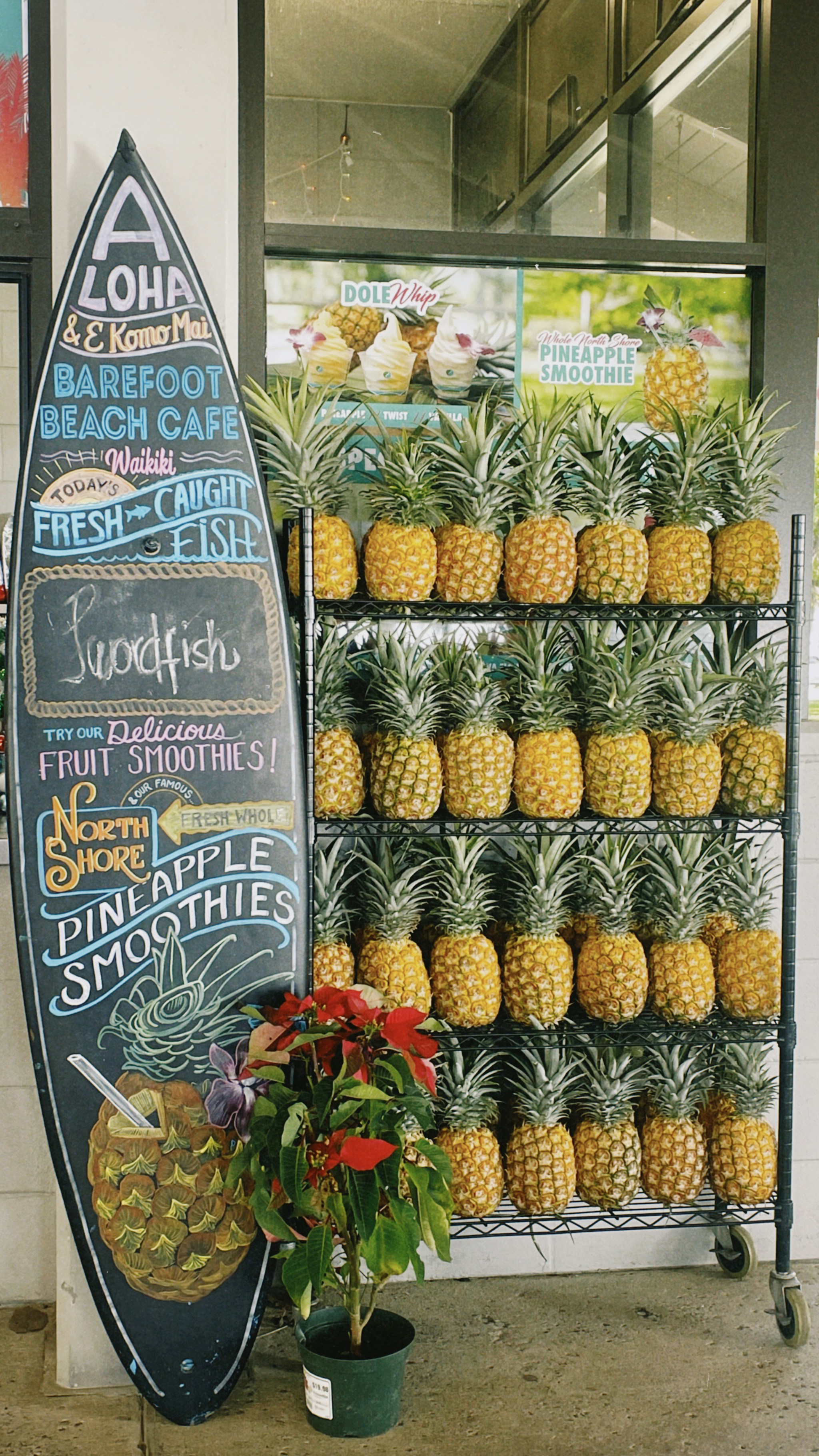 Ananas esposti sugli scaffali accanto a un cartello per una tavola da surf