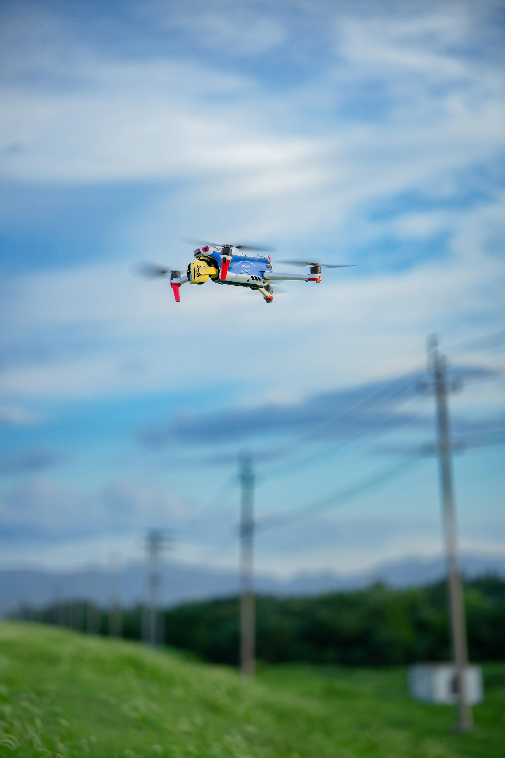 A drone flying over a green field with power lines.