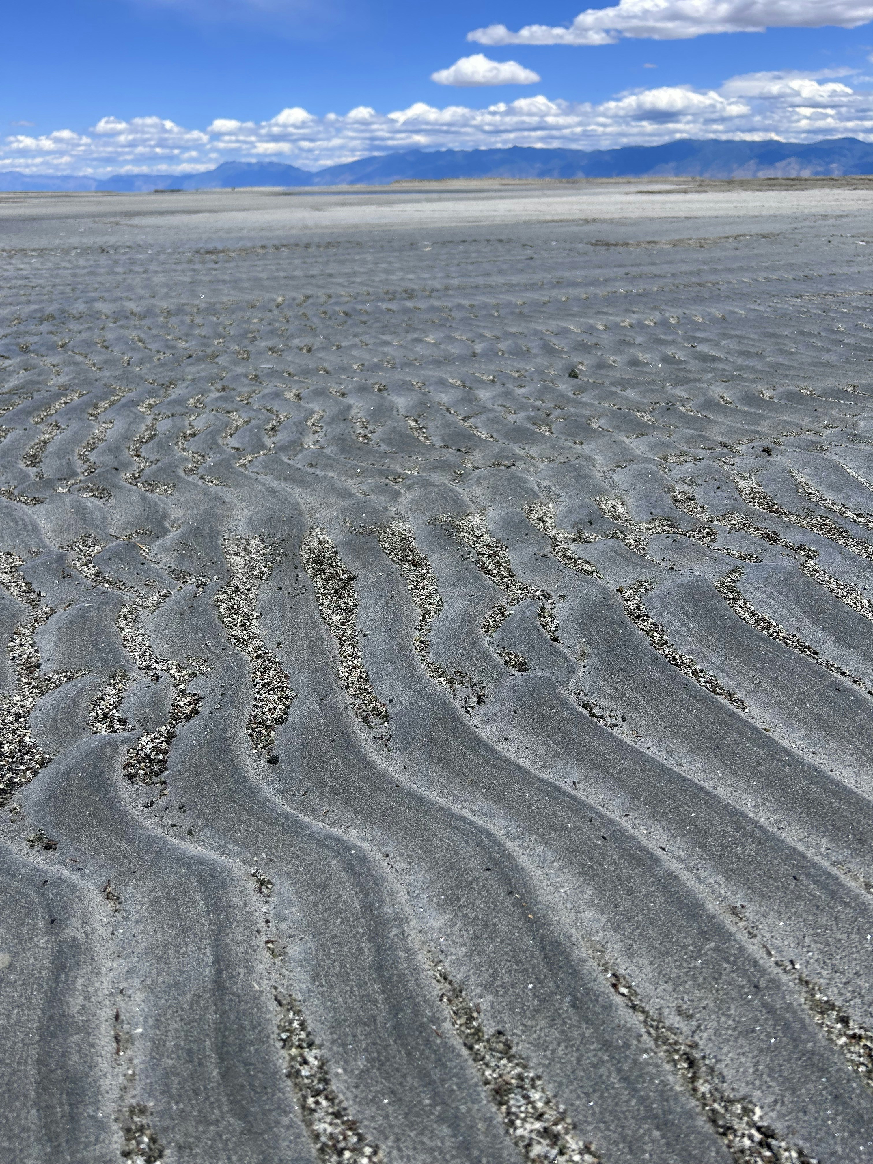 Wavy sand patterns on a beach under a blue sky.