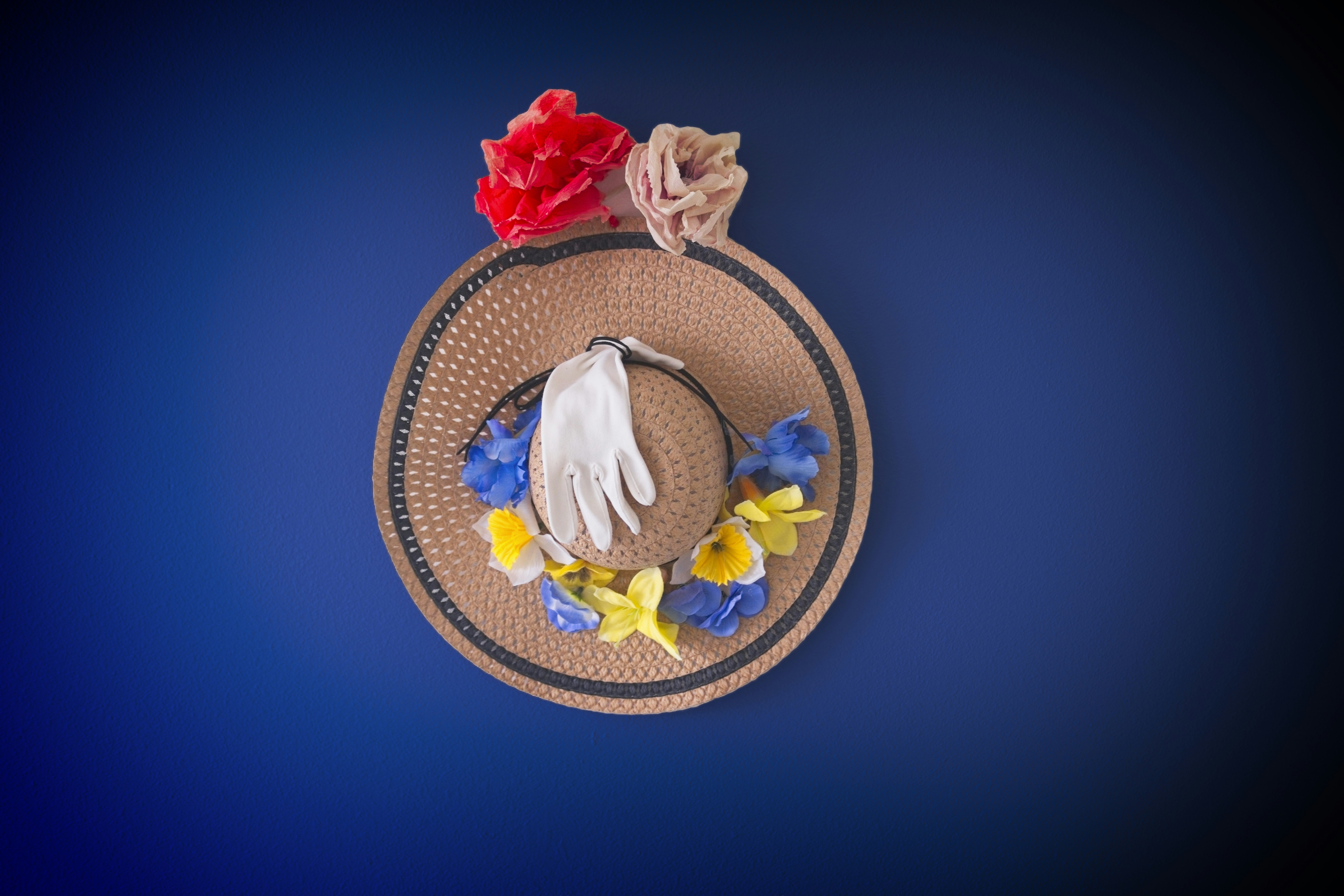 A decorated straw hat with flowers and a white glove.