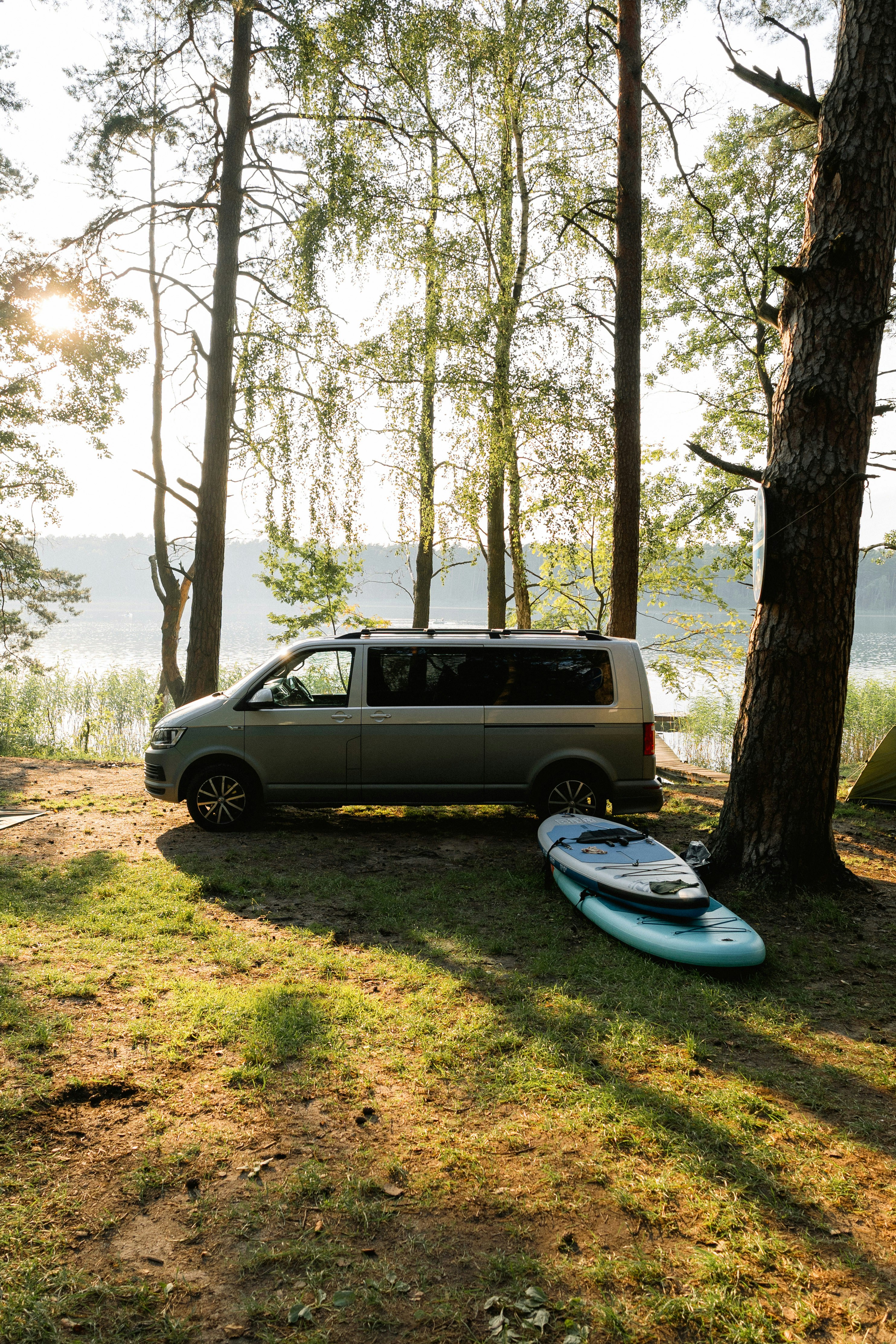 Van and paddleboard by lake in sunlit forest