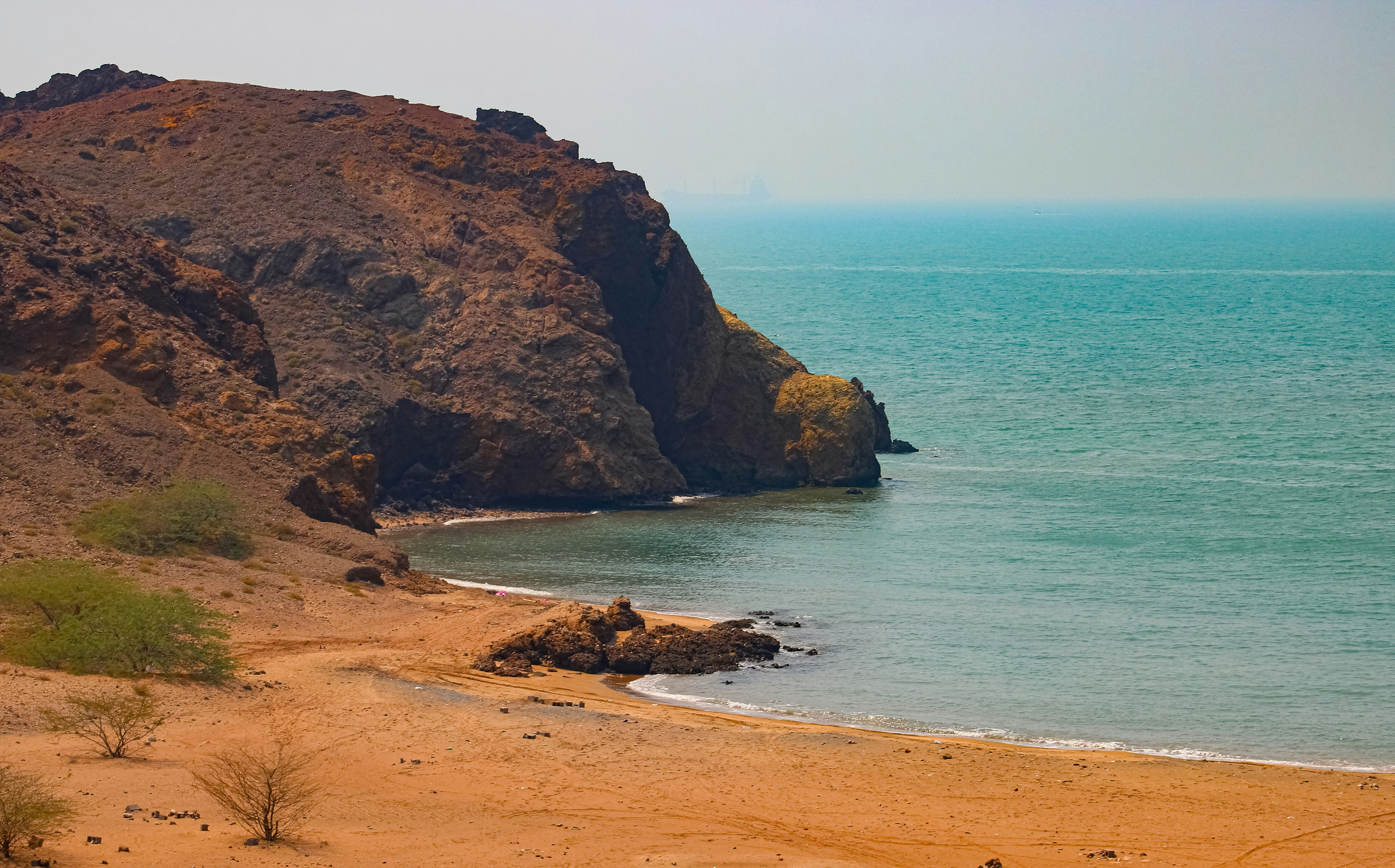 Rocky cliff overlooks a sandy beach and turquoise ocean.
