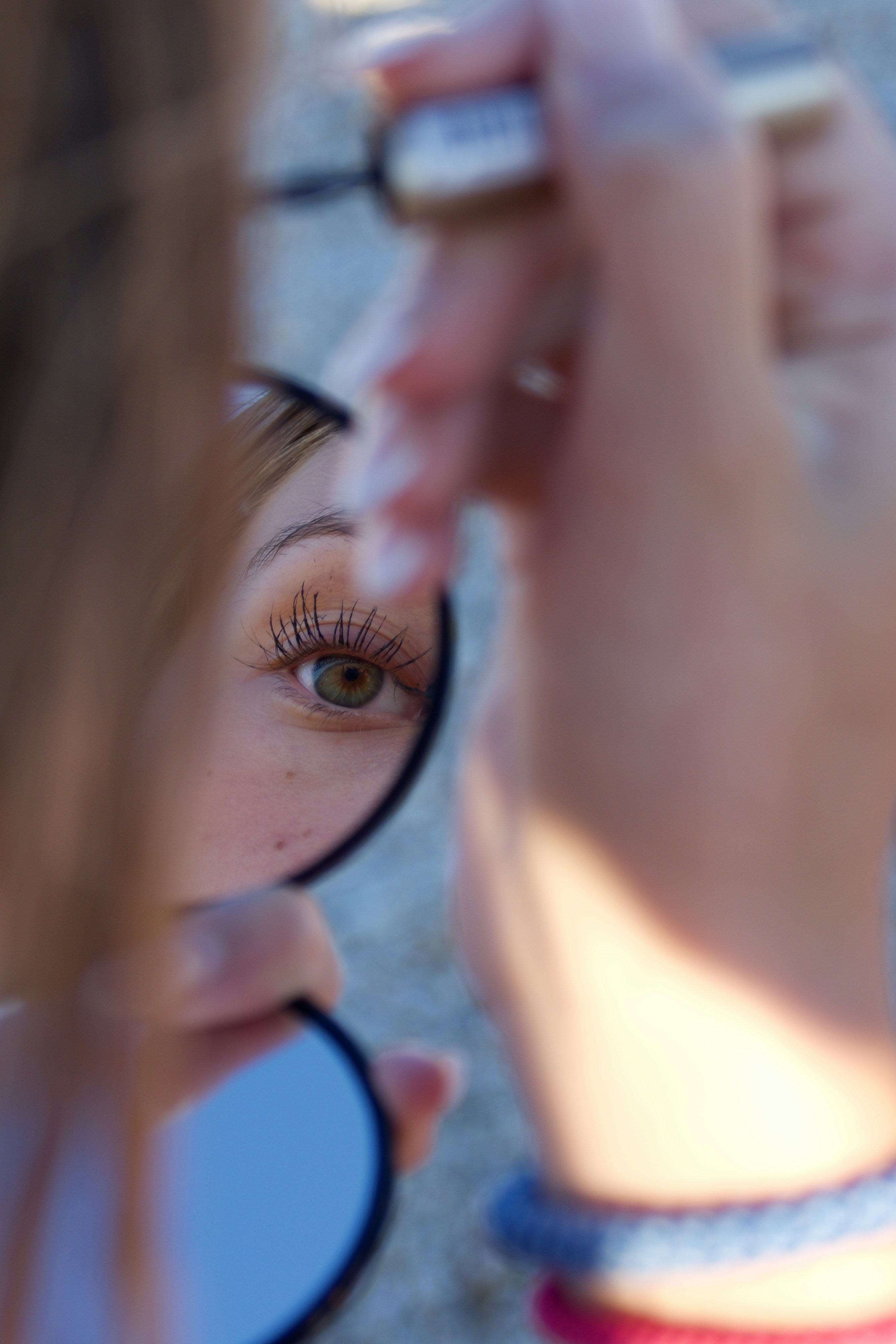 Person applying mascara, reflected in a small mirror.