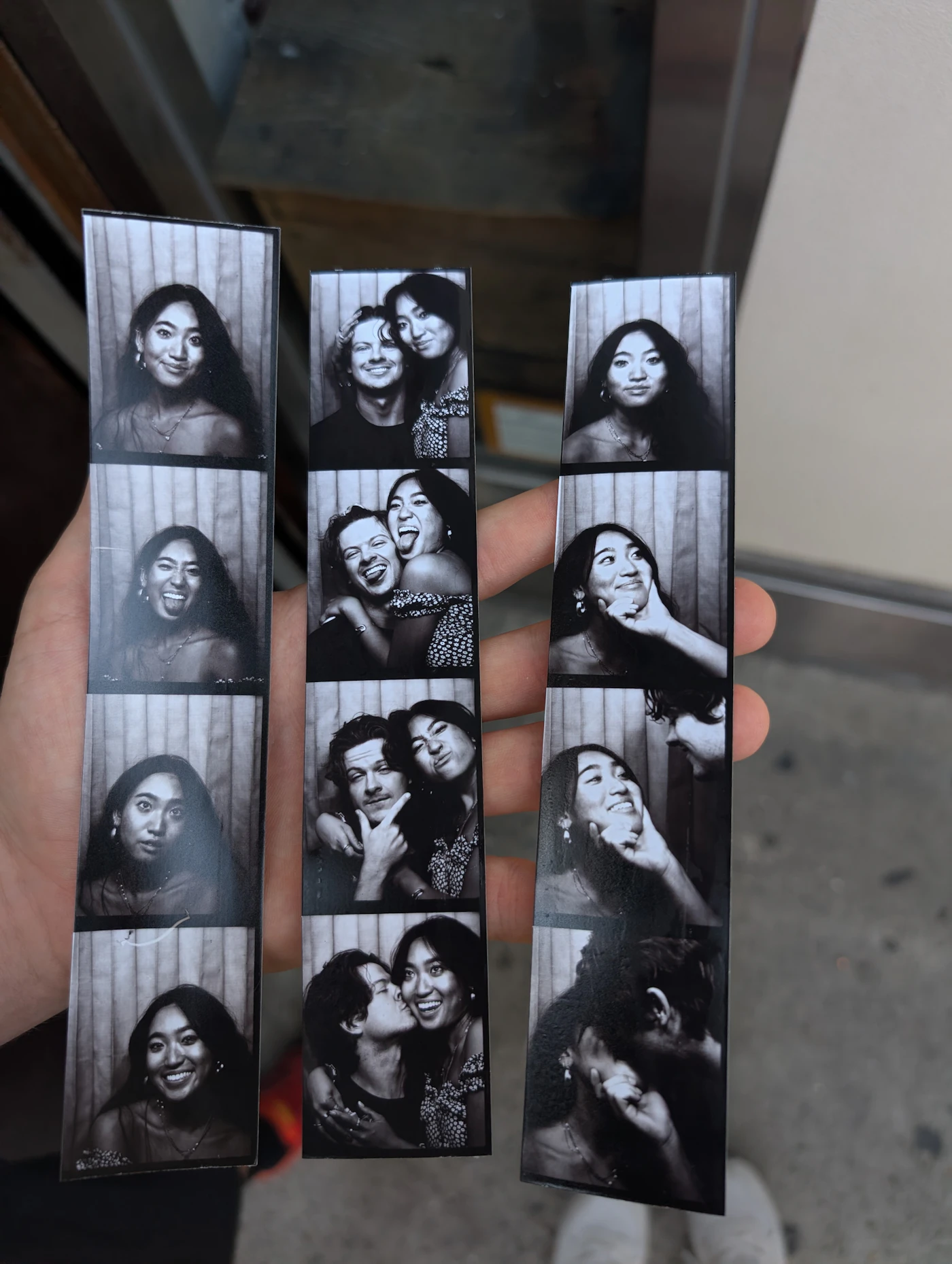 A hand holding three black-and-white photo booth strips