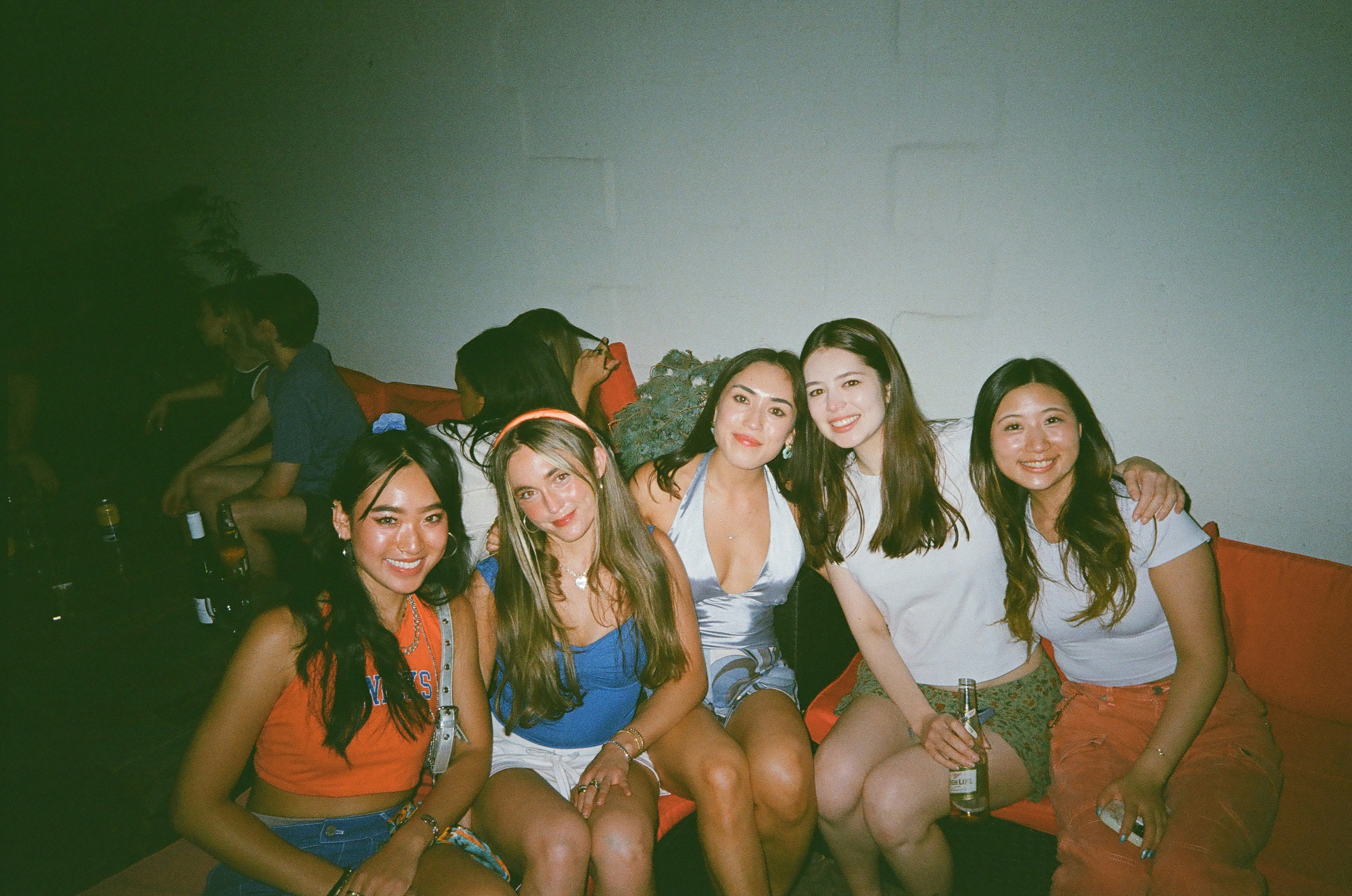 Cinco jovens sorrindo juntas em uma festa com pouca luz