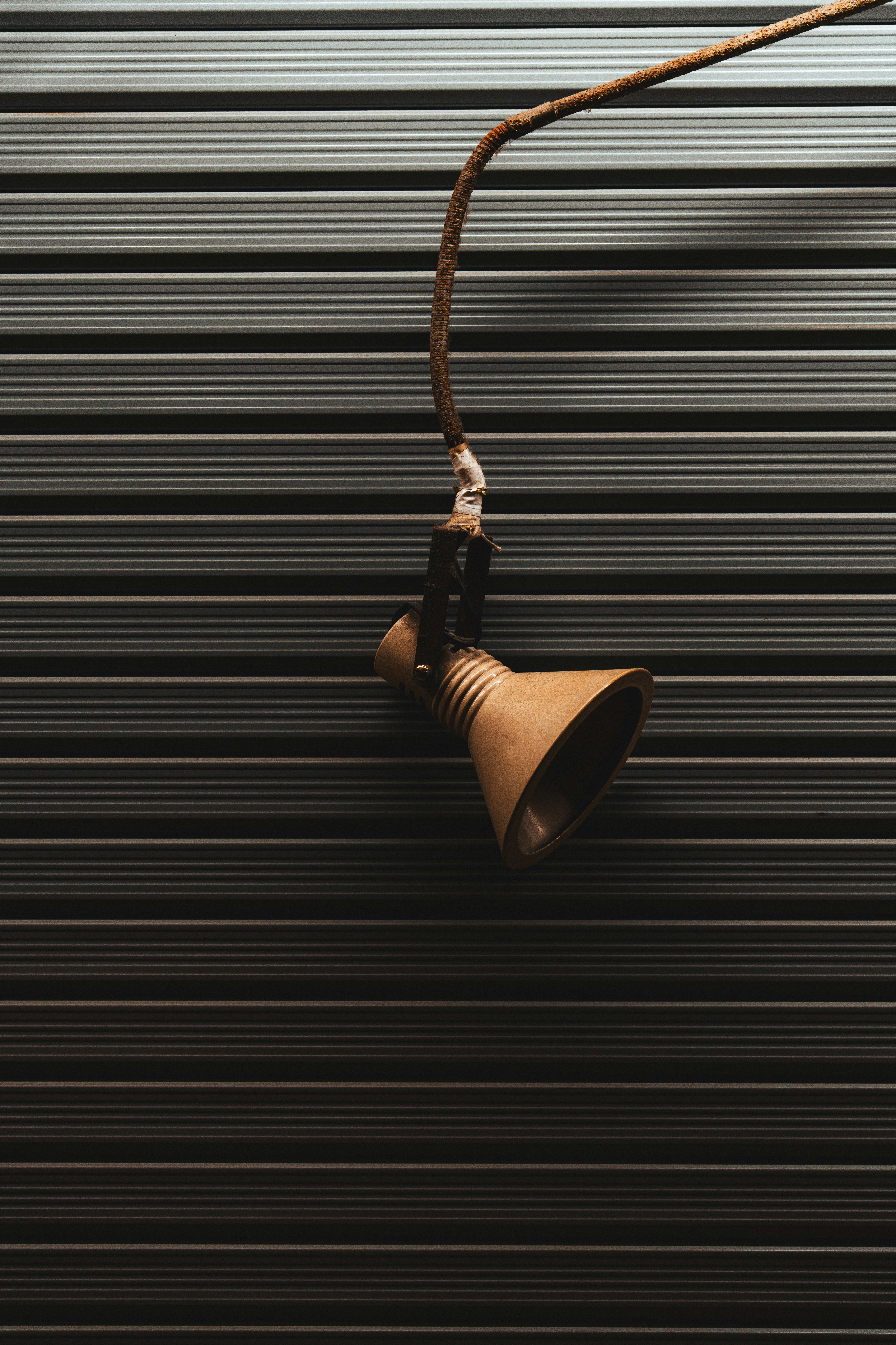 A hanging brown light fixture against a dark striped background.