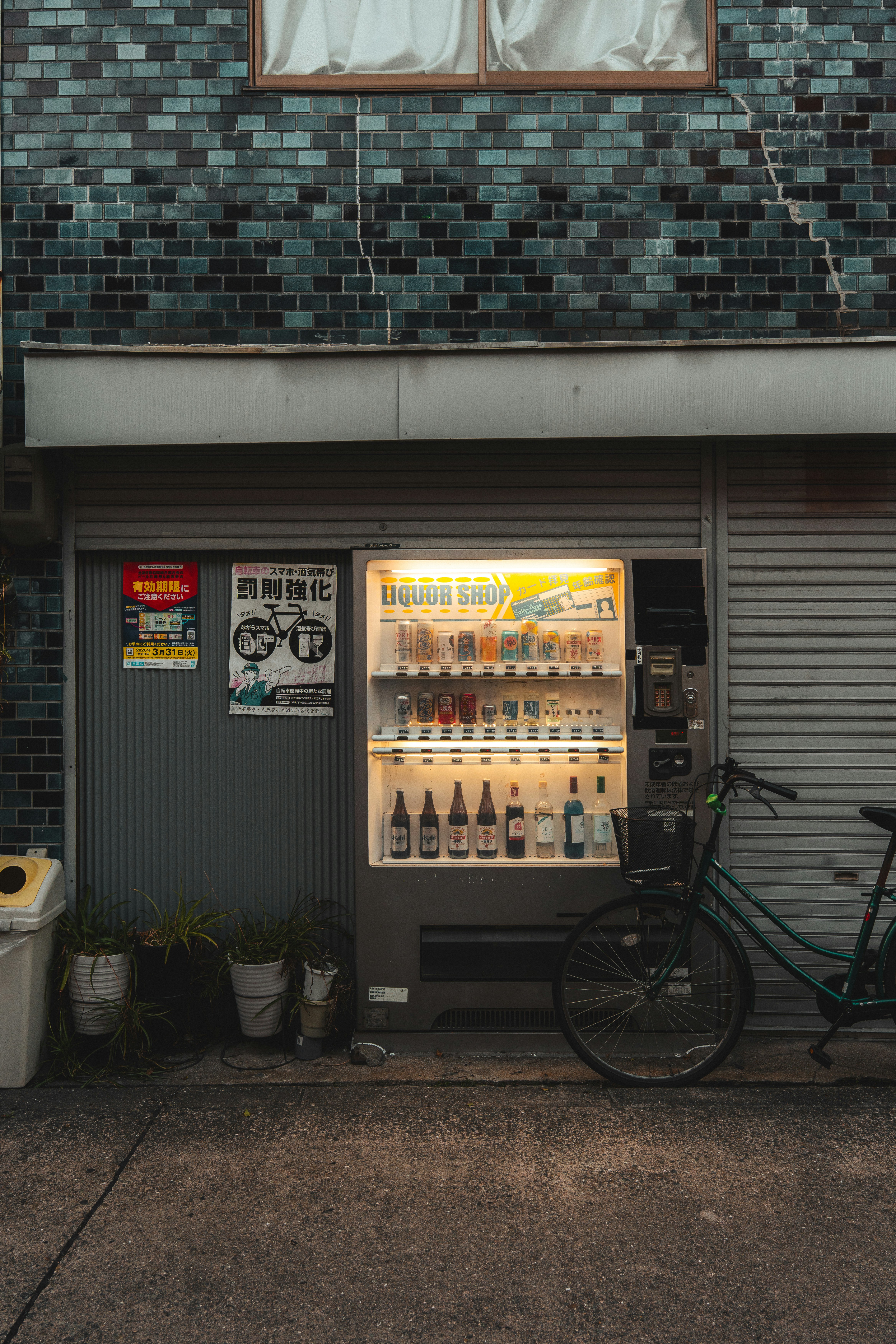 Illuminated liquor vending machine with a bicycle parked outside.