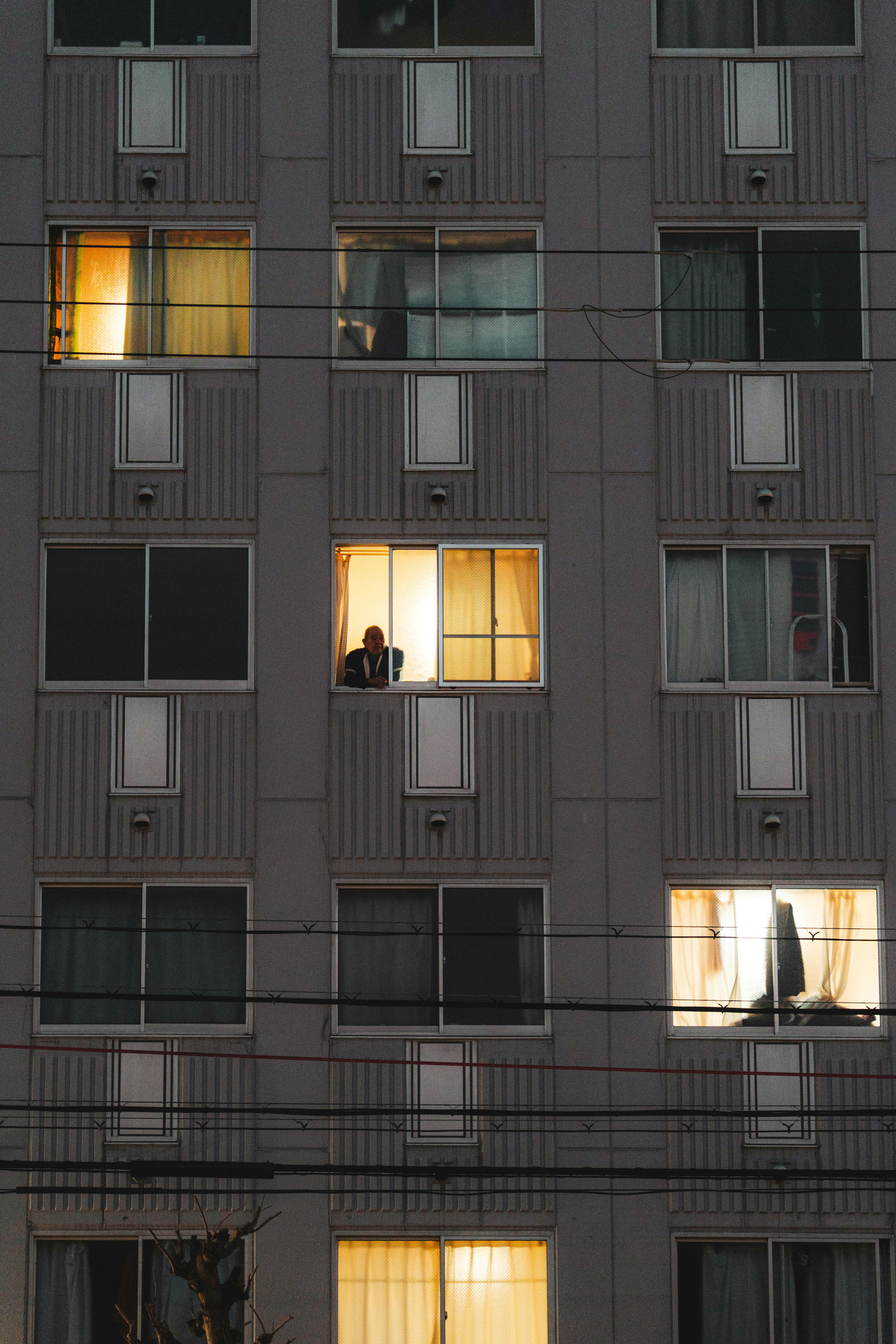 A person looks out from a brightly lit apartment window.