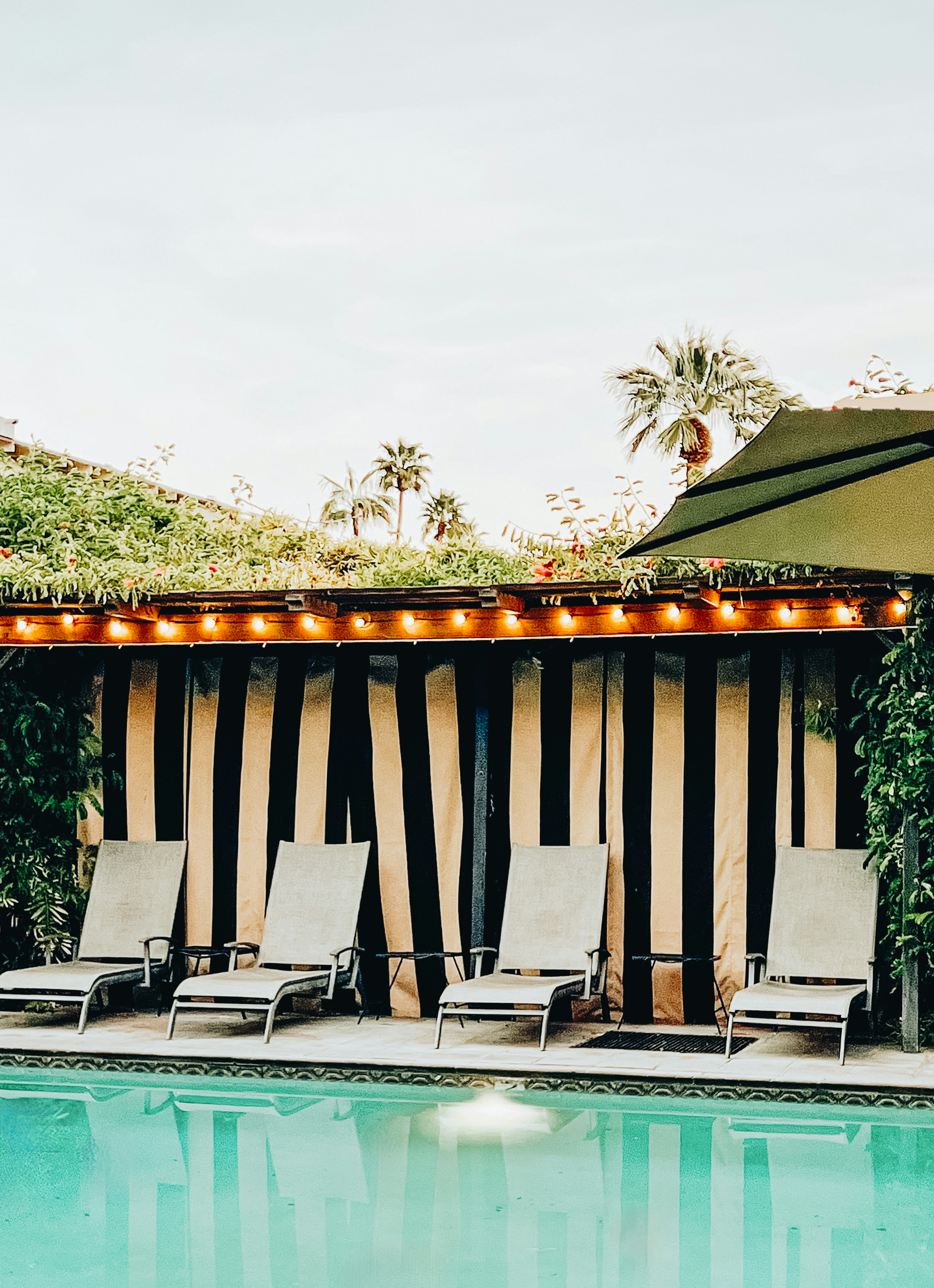 Lounge chairs beside a Palm Springs pool with a striped cabana