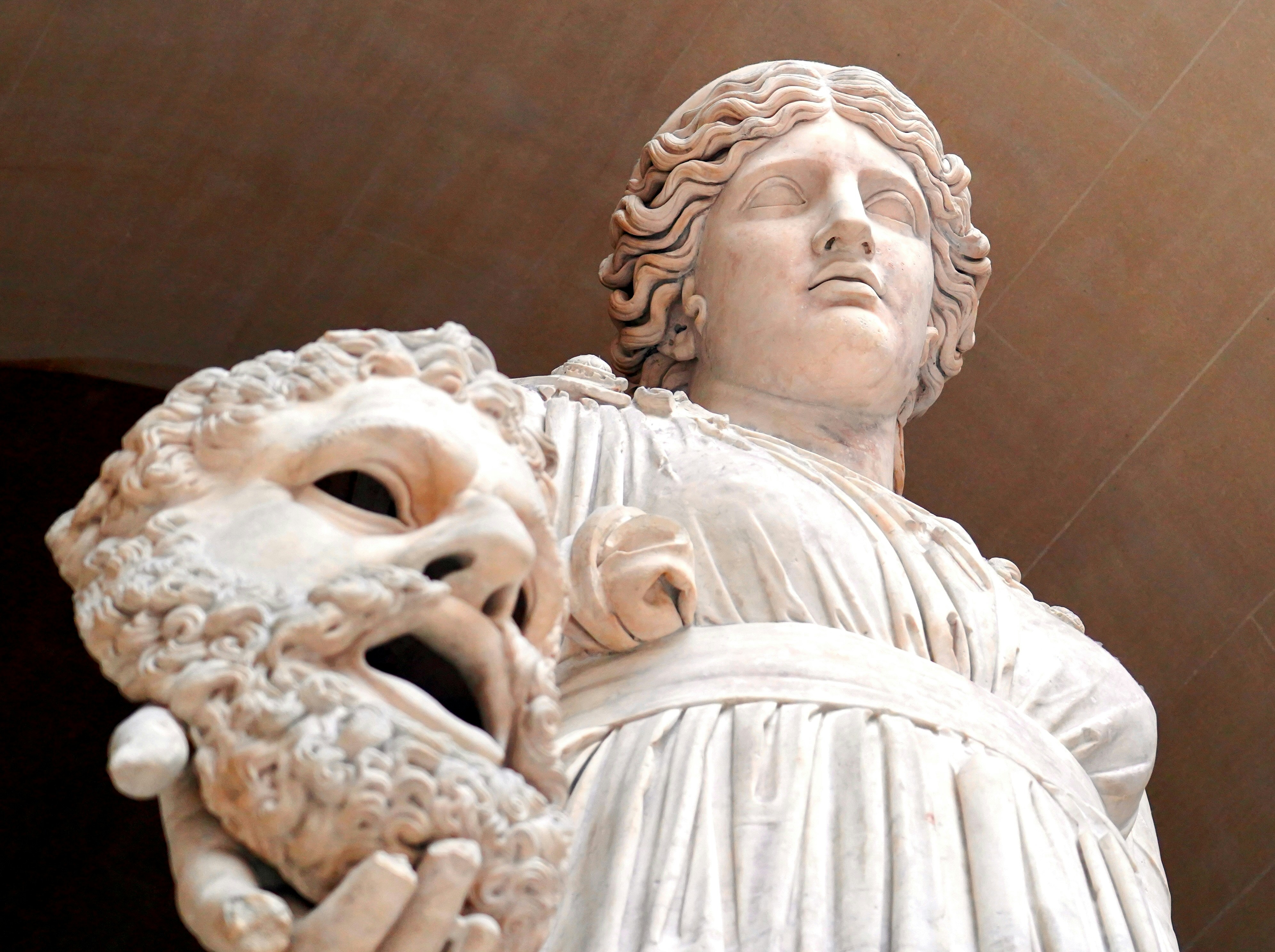Statue en marbre blanc d’une femme tenant un masque théâtral.