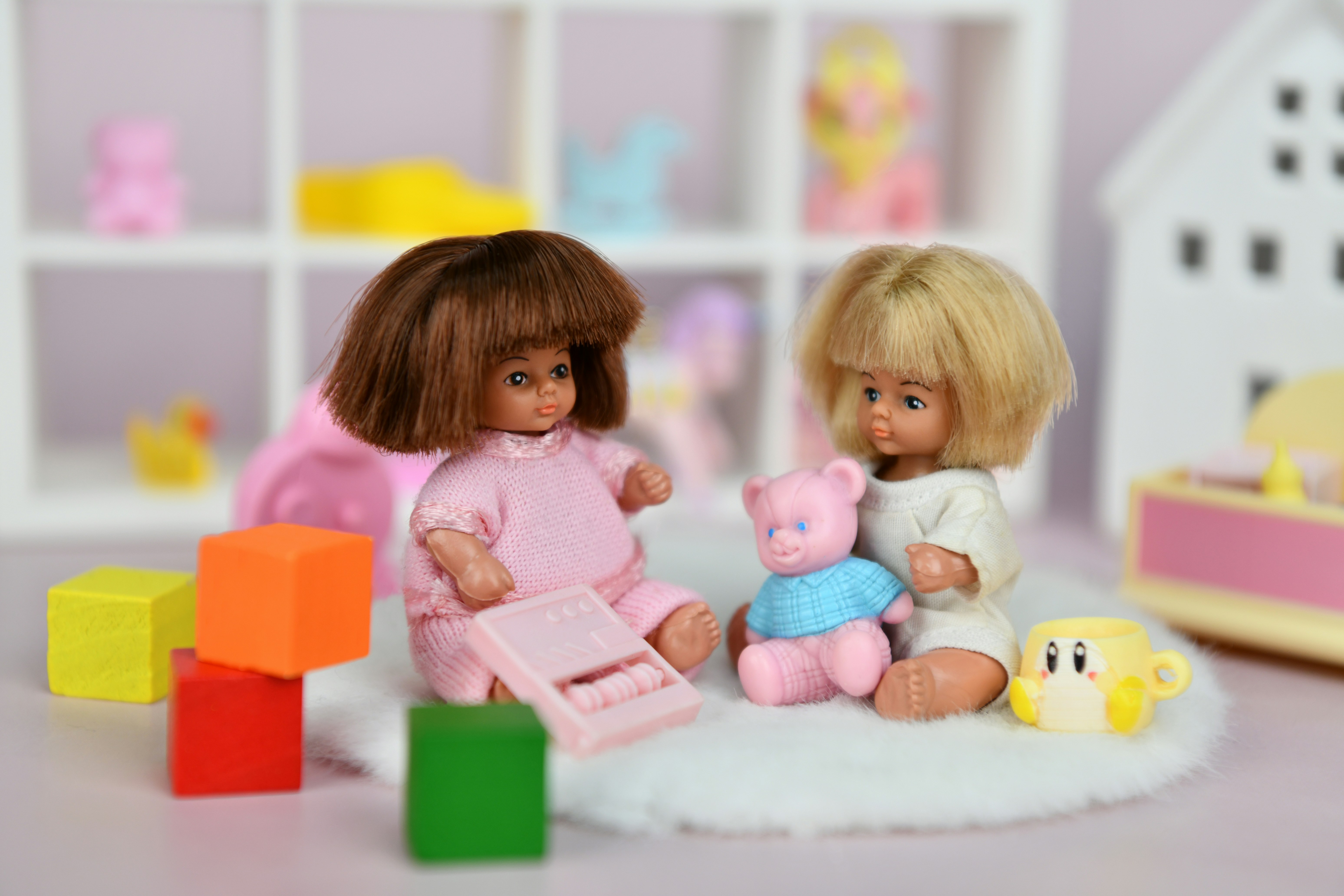 Deux poupées jouant avec des blocs et un ours en peluche.