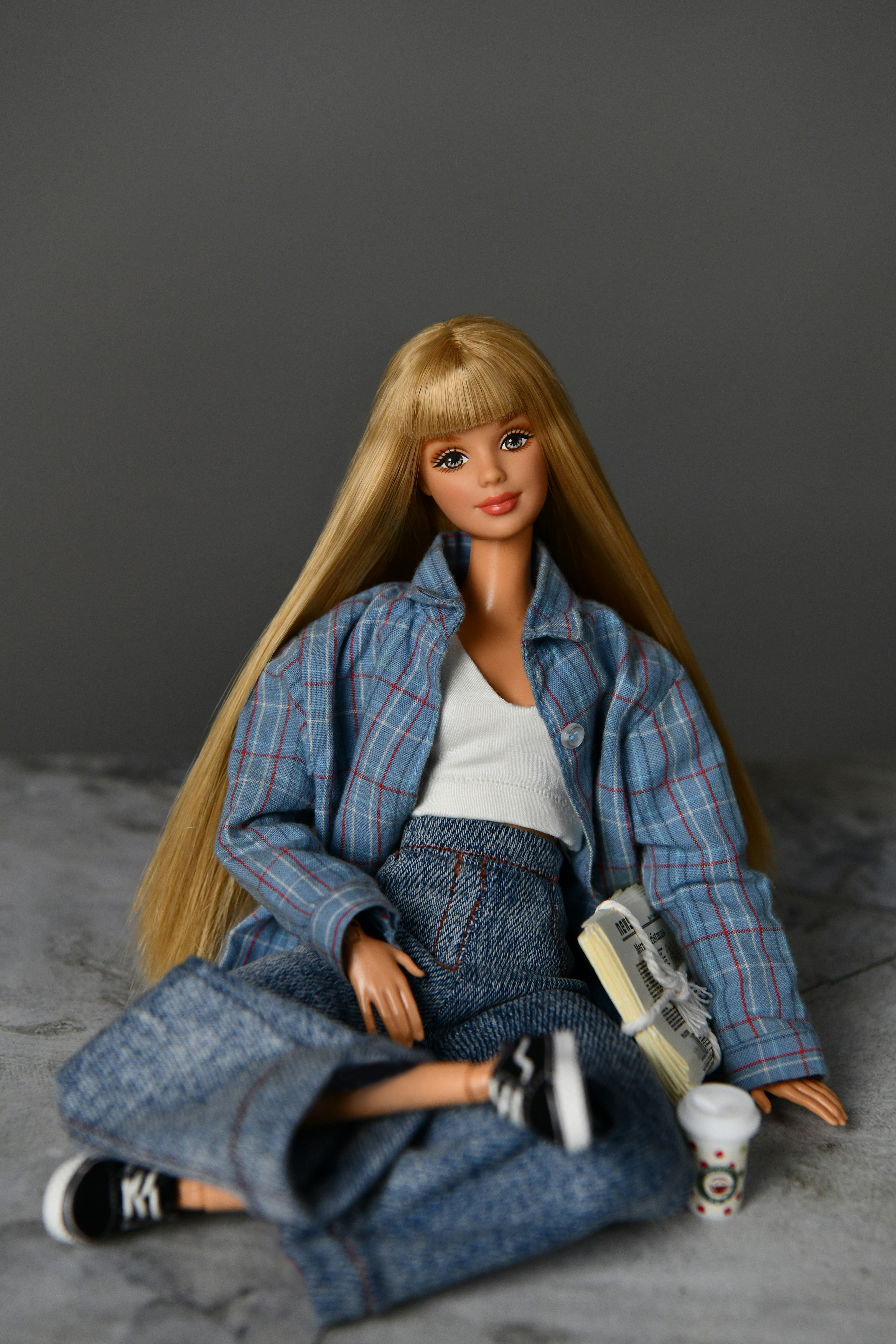 Poupée blonde en veste à carreaux, jean et baskets avec du café.