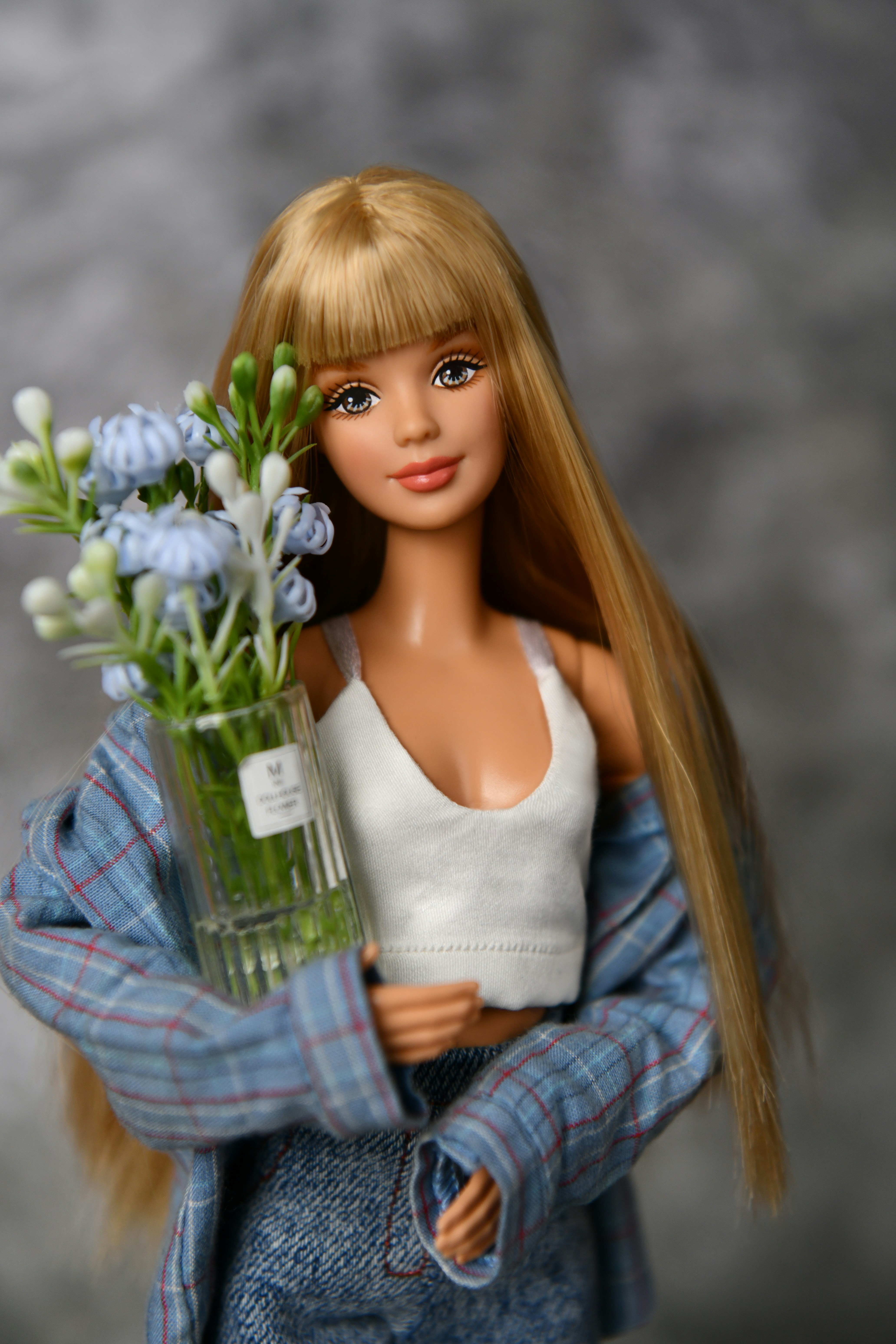 Poupée blonde tenant un vase de fleurs bleues et blanches.