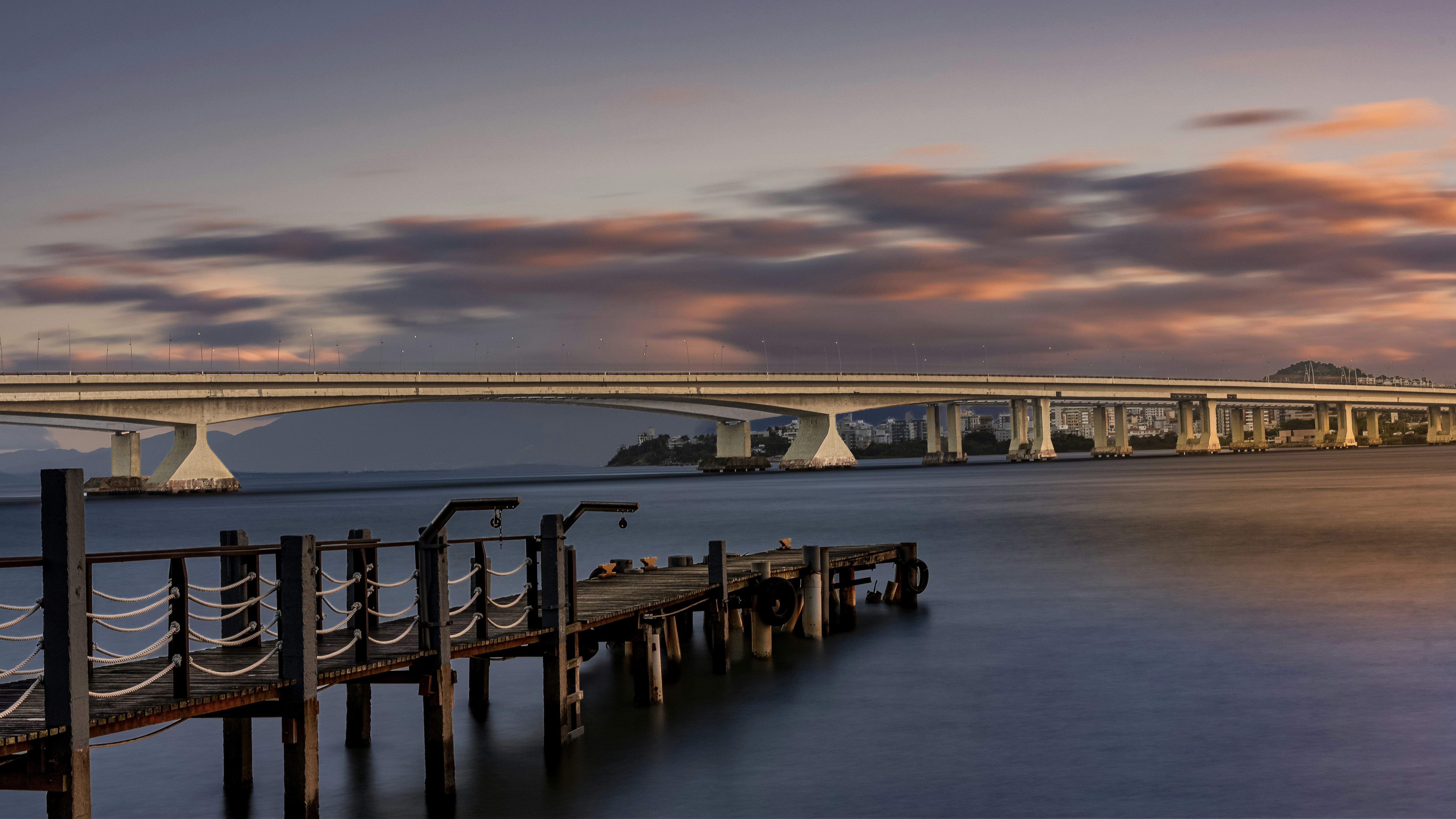 Old wooden pier and bridge over water at sunset