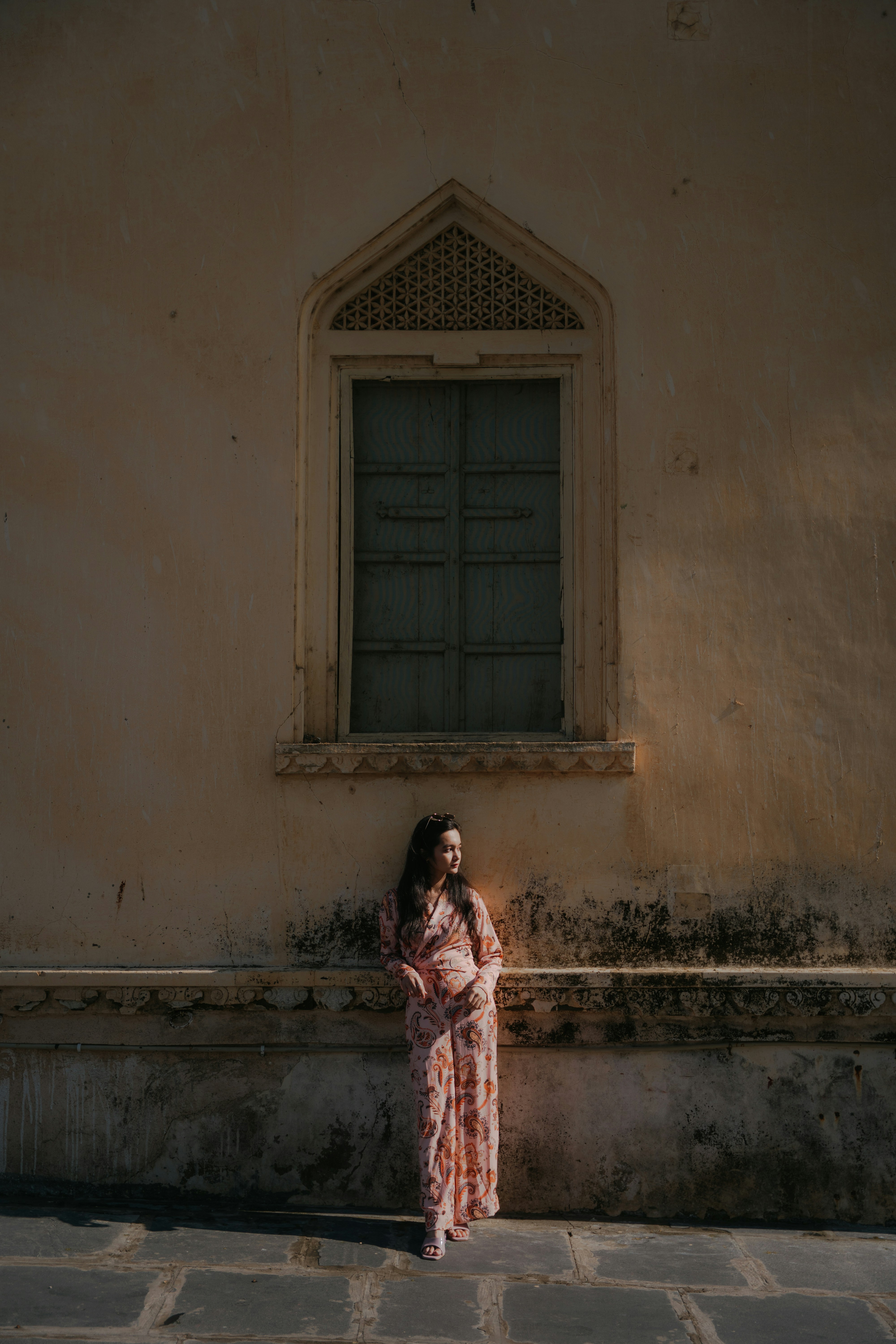 Woman in patterned dress standing by an ornate window.