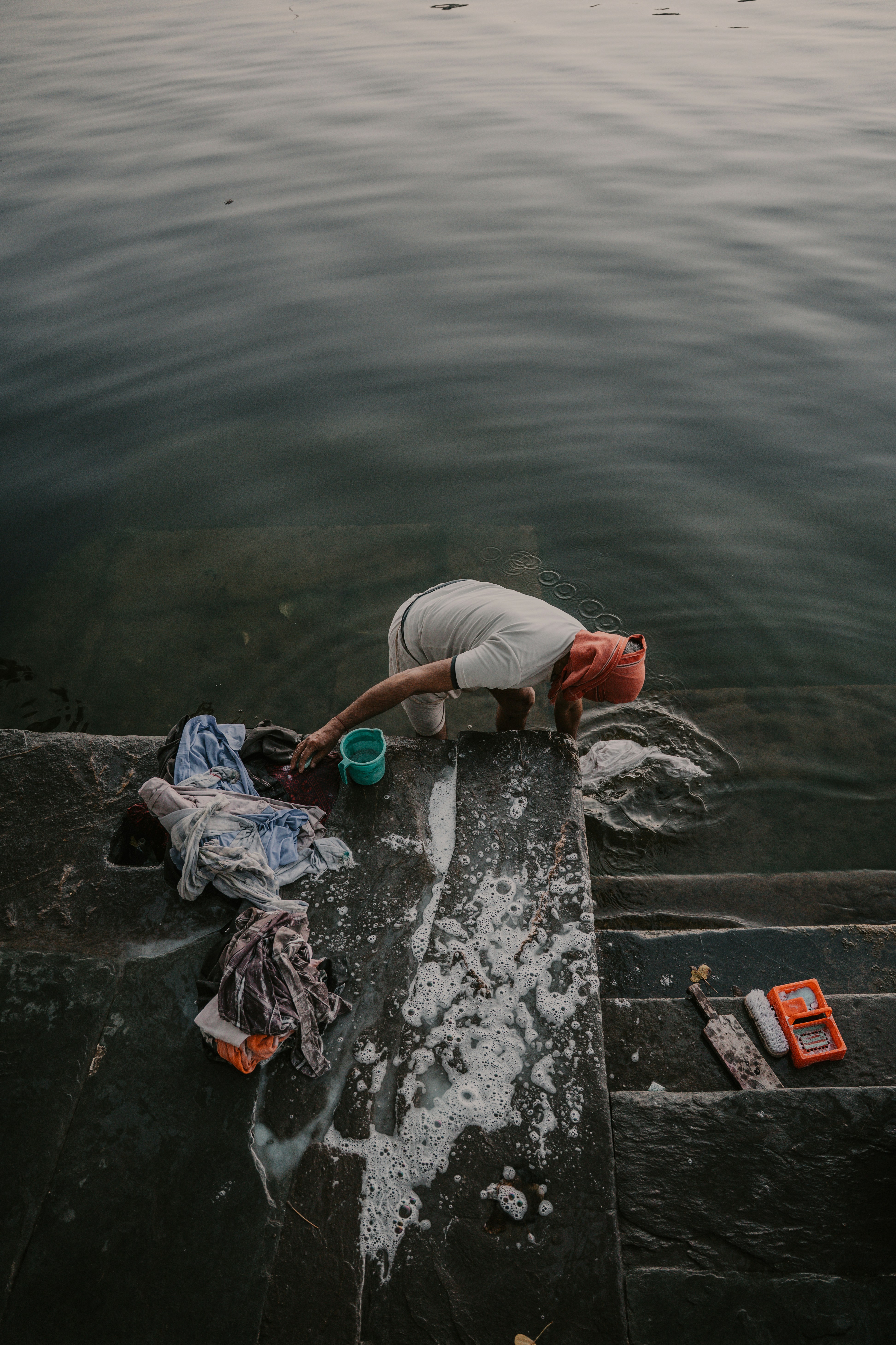 A person washing clothes in the water on stone steps.