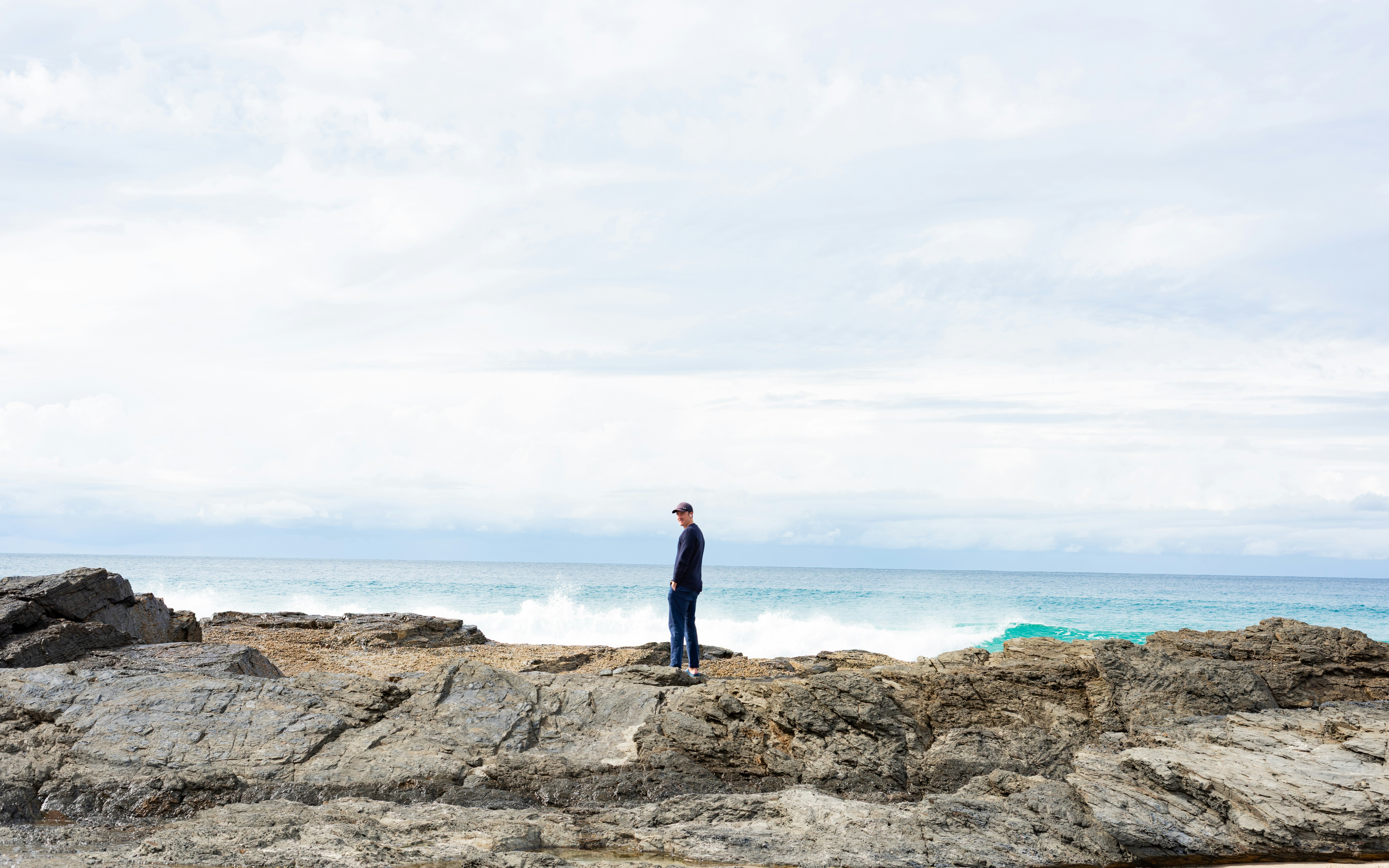 A person stands on rocky shore looking at the ocean