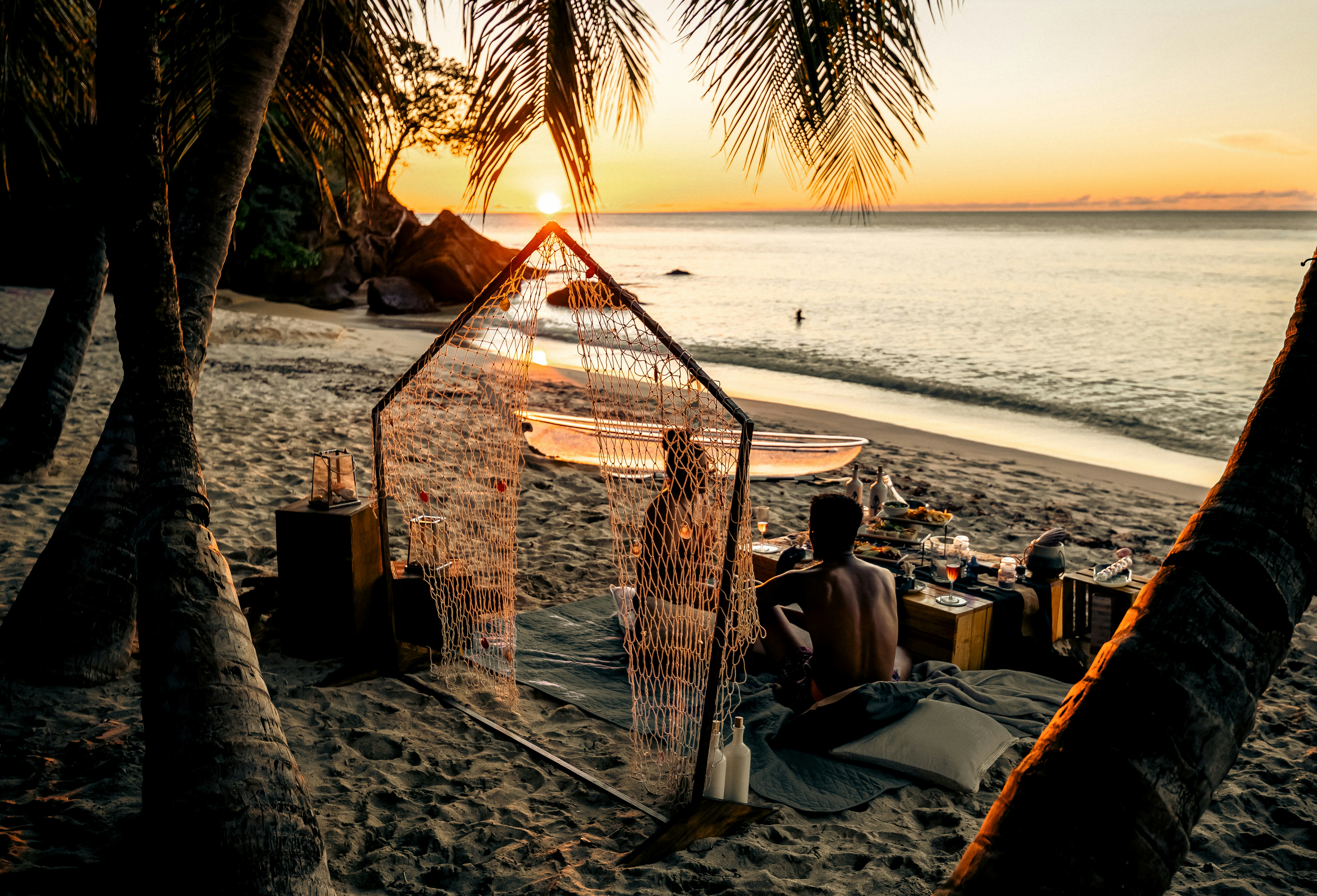 La persona si gode il tramonto su una spiaggia tropicale con palme.