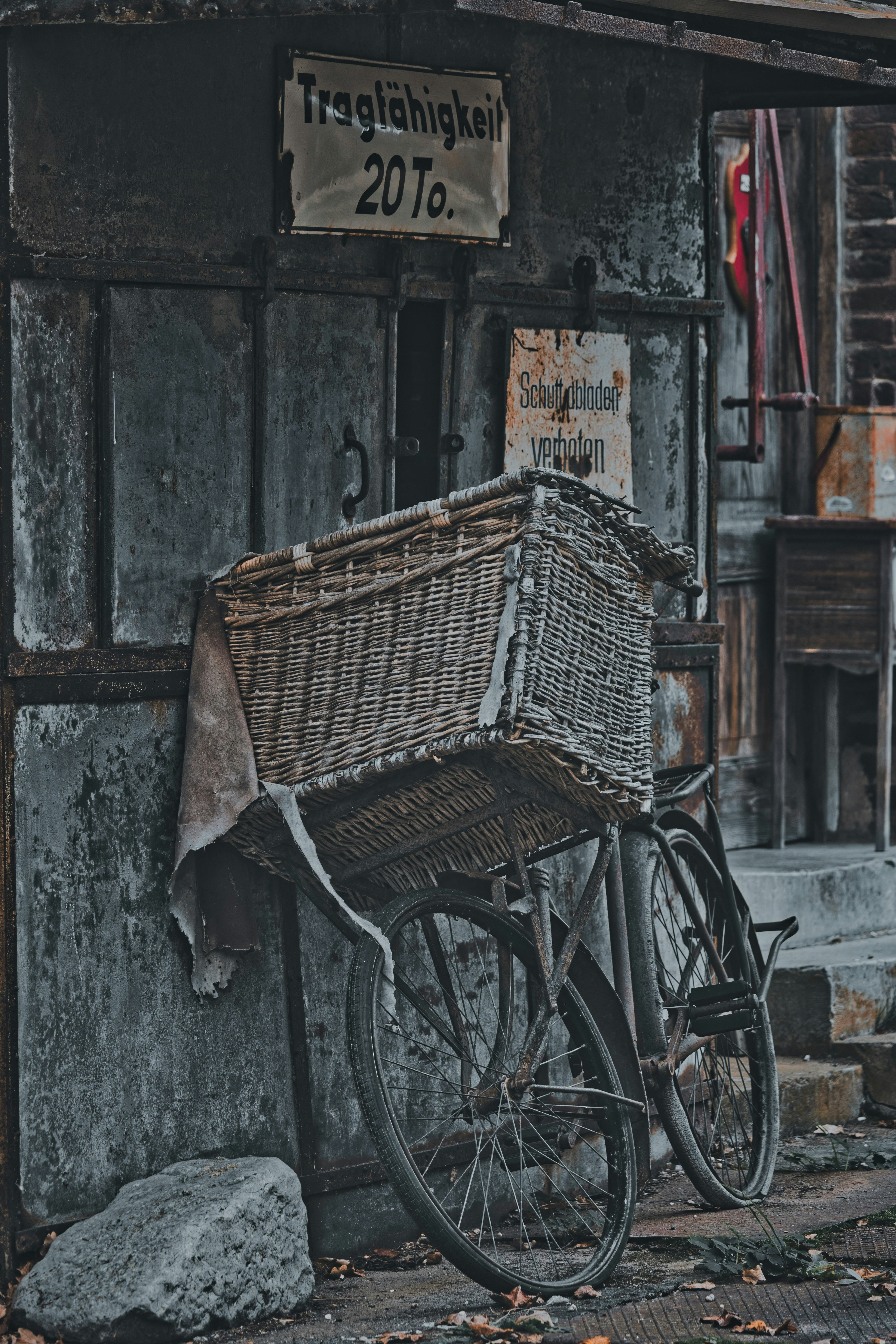 Wicker basket bicycle leans against a rustic, dark building.