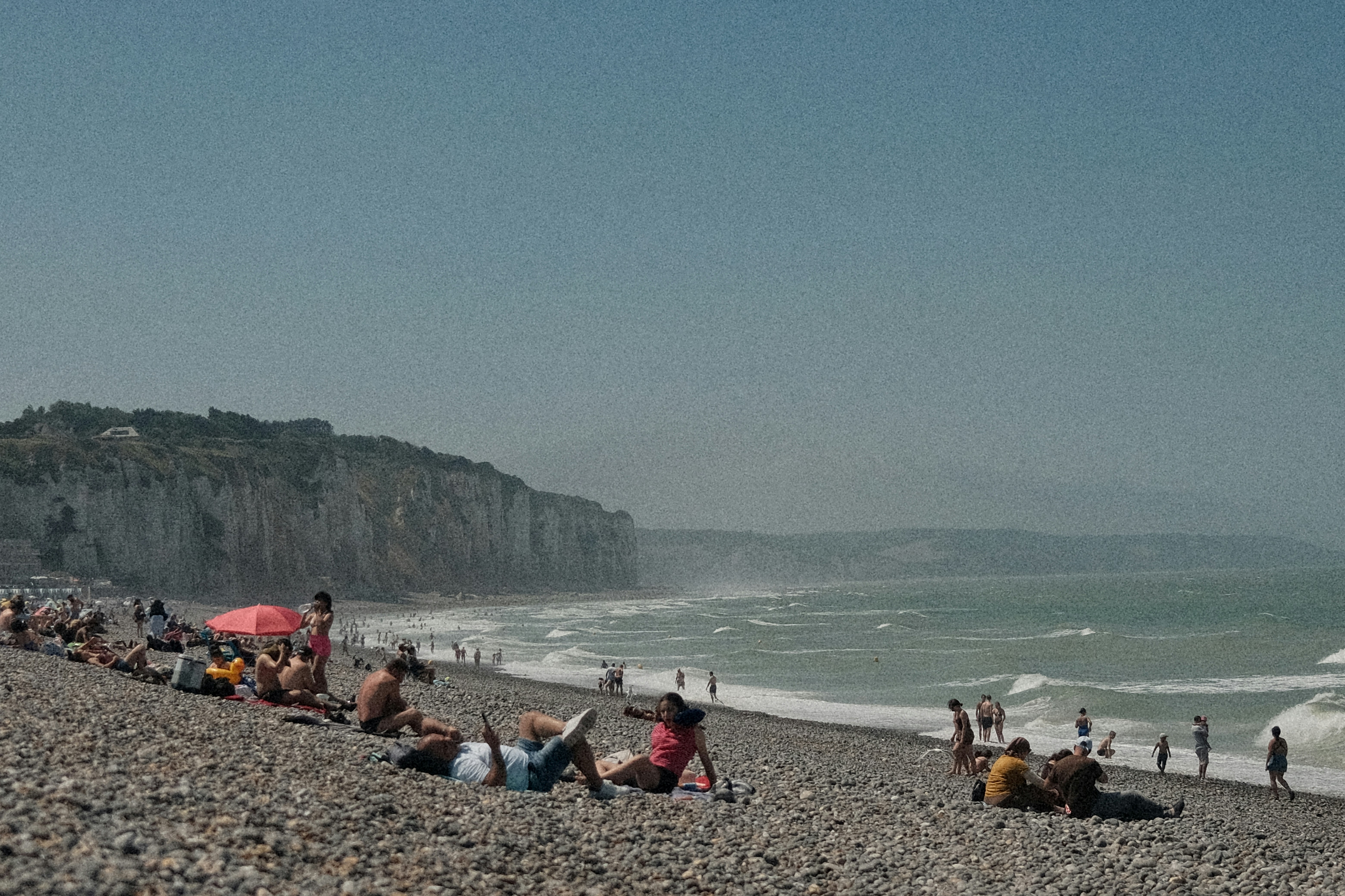 People relax on a pebbled beach beside cliffs and ocean