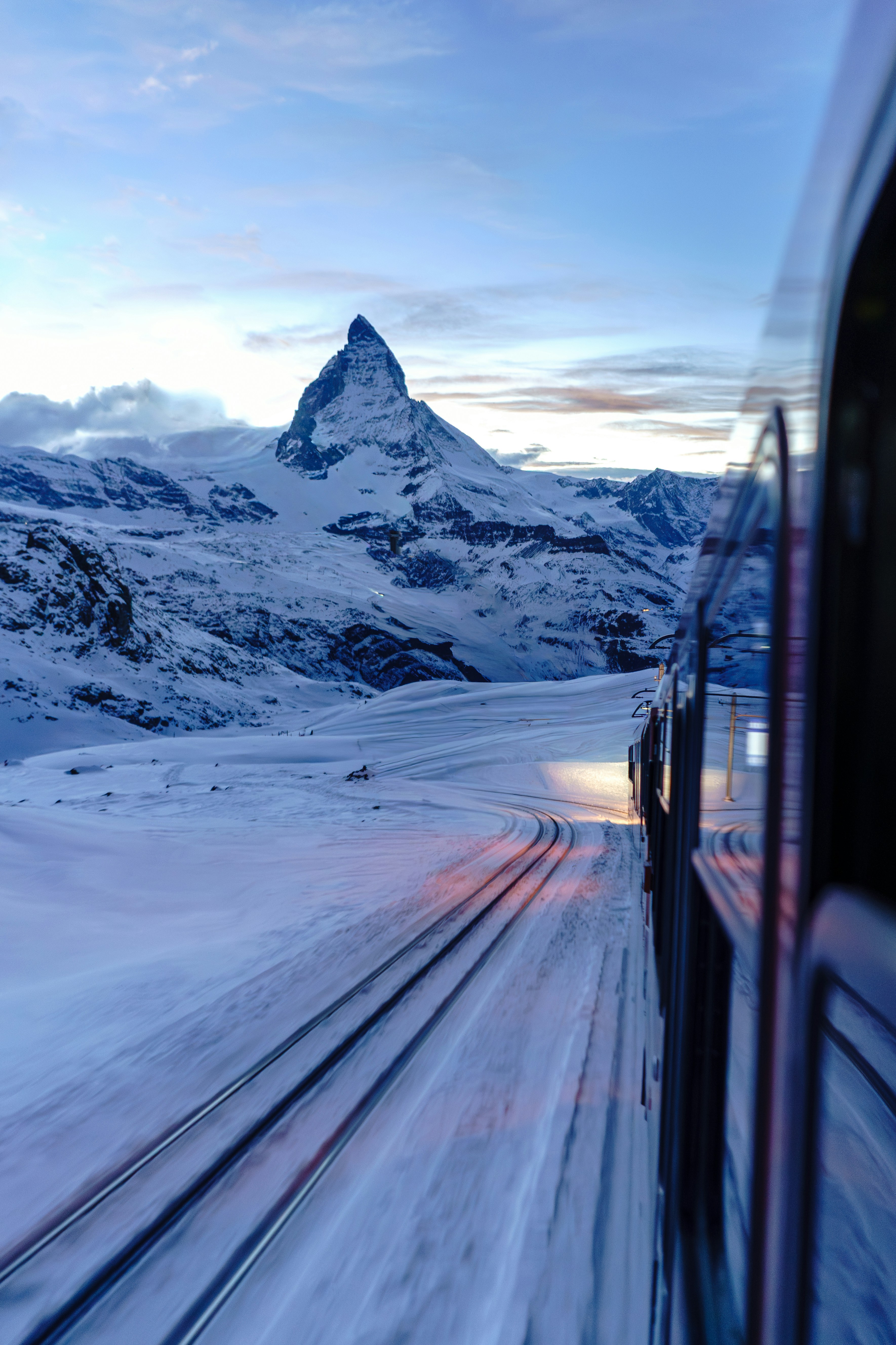 Train traveling through snowy mountains towards matterhorn.