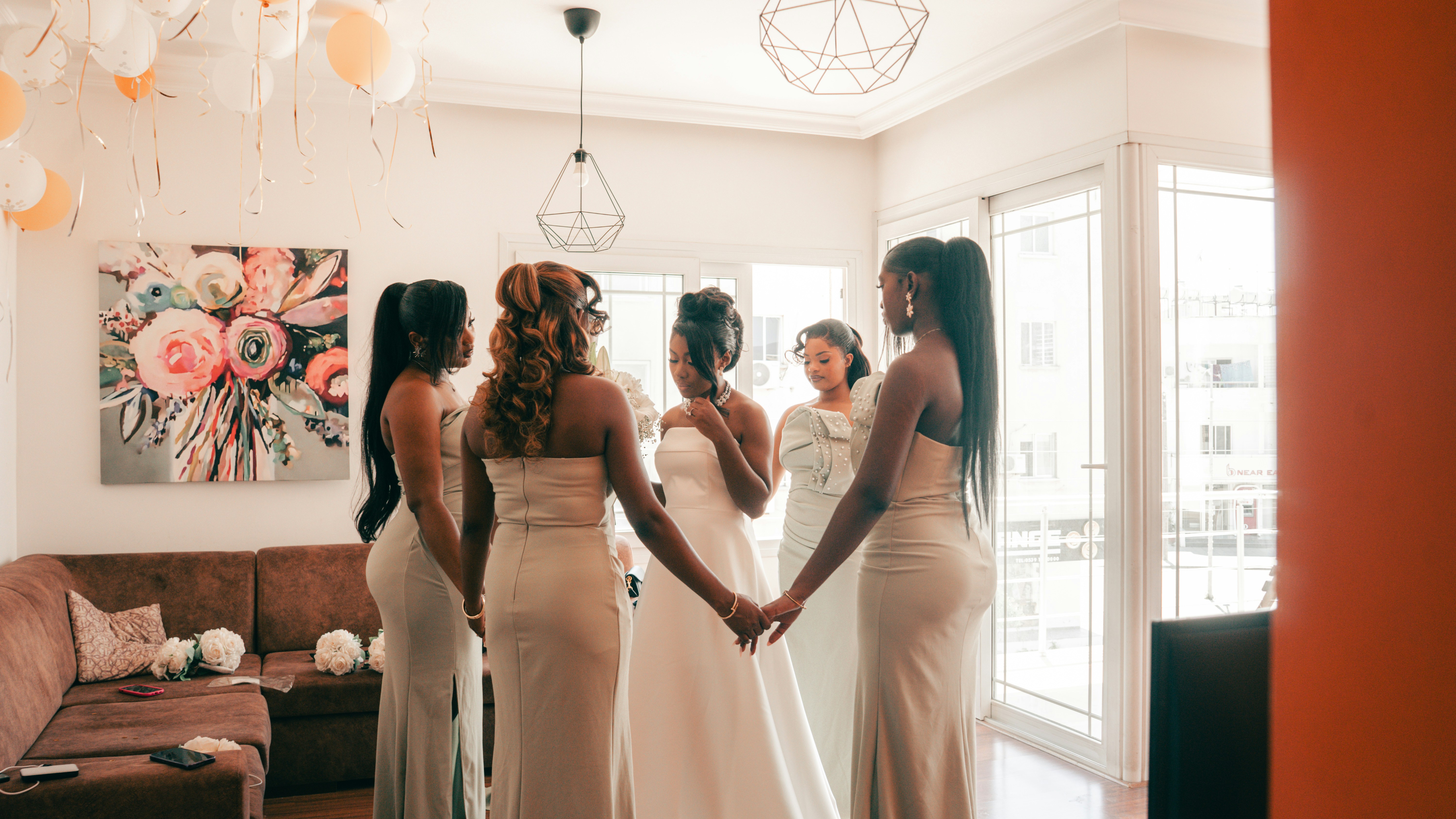 Bride and bridesmaids holding hands in a celebratory room.