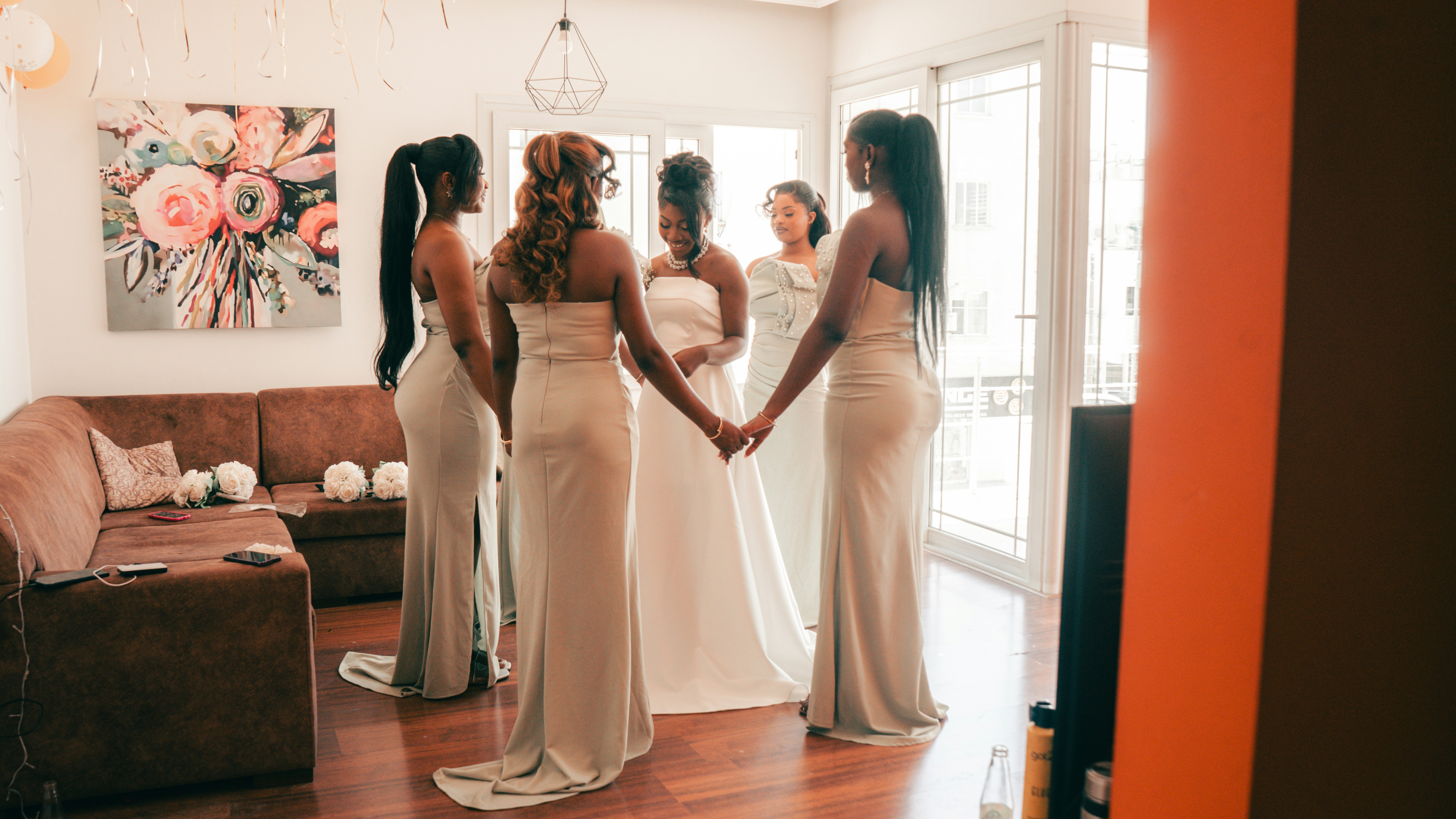 Bride and bridesmaids holding hands in a bright room.