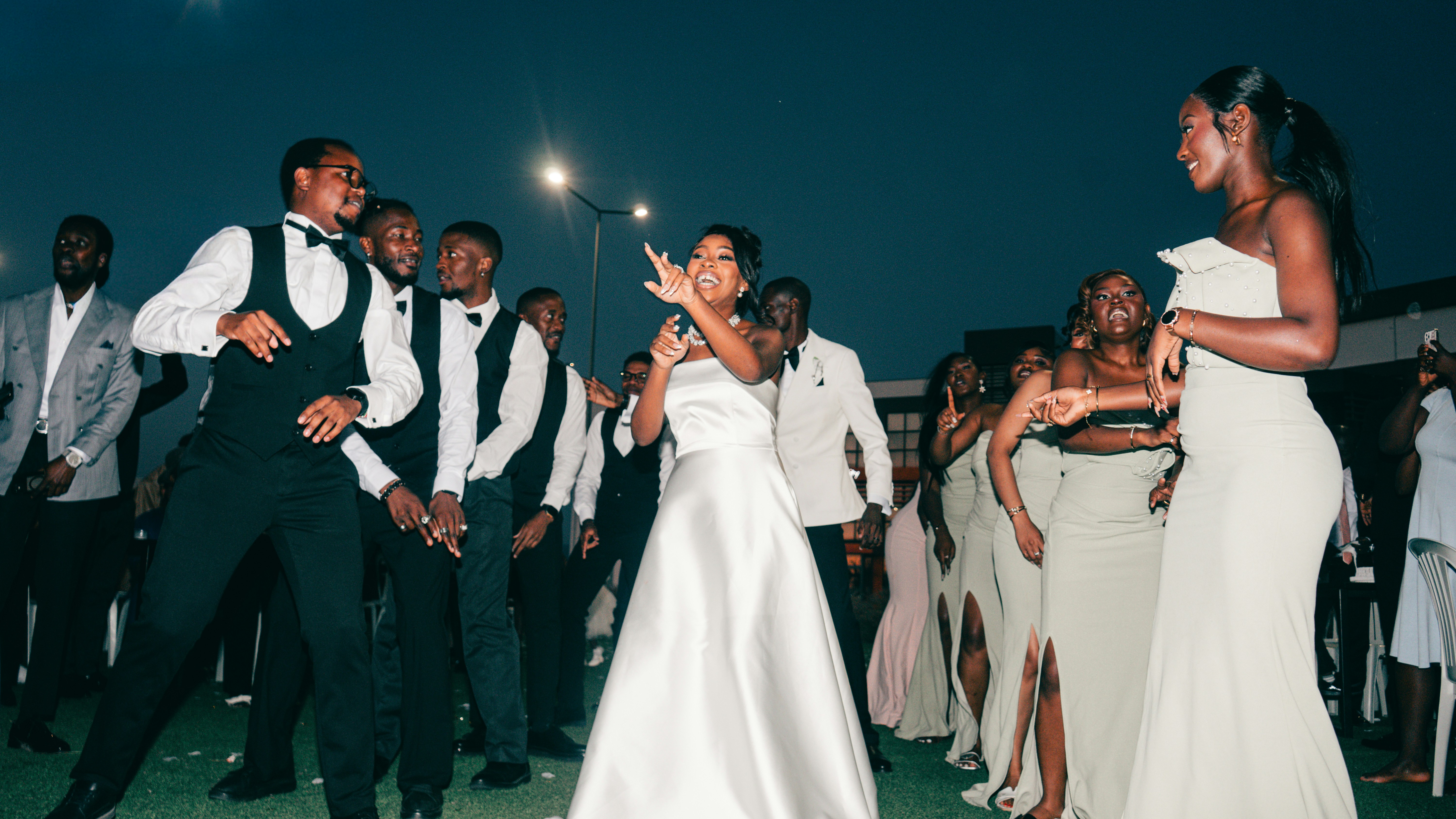 People in formal attire dancing energetically outdoors at night.