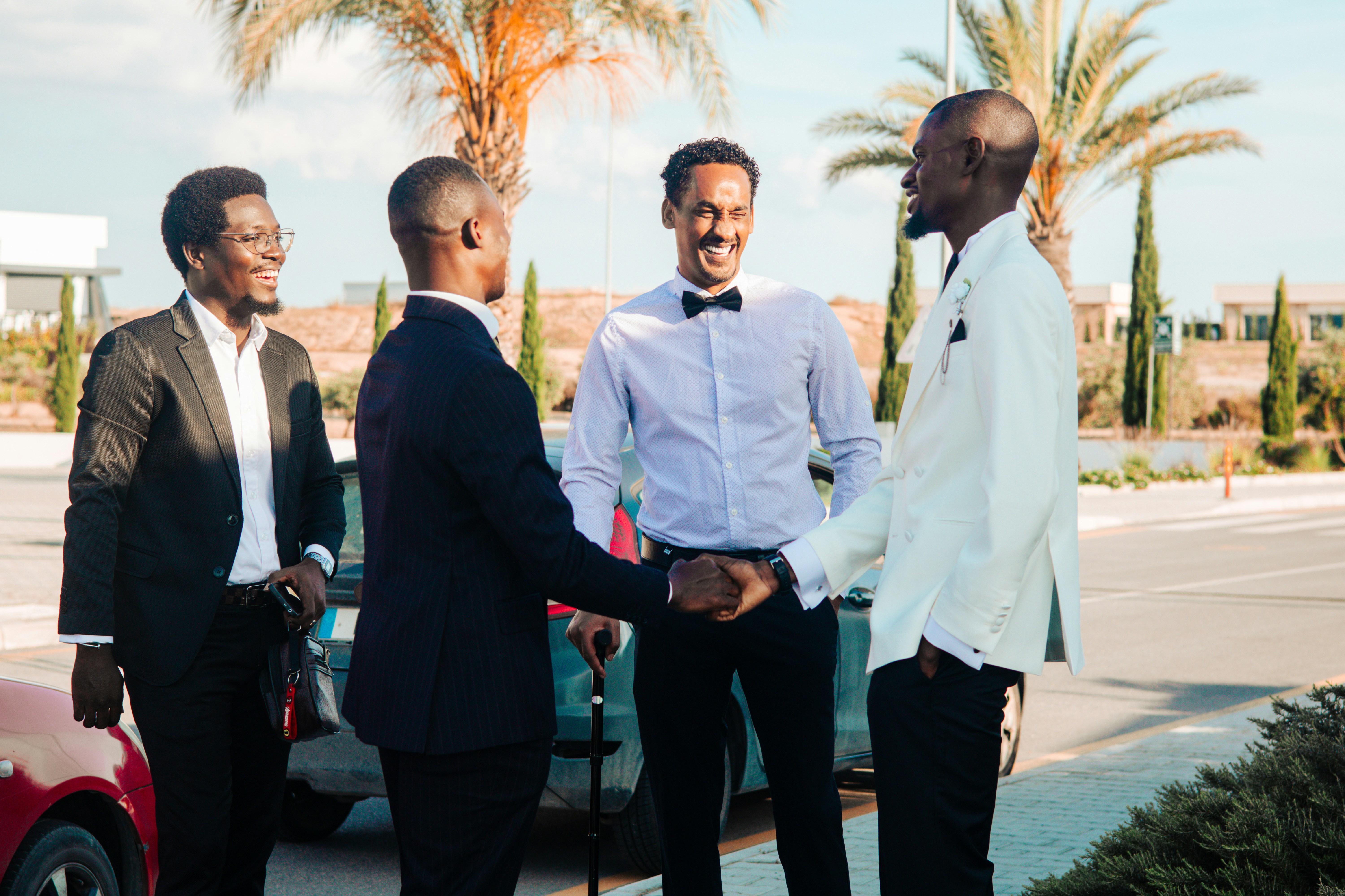 Four formally dressed men shaking hands outdoors.