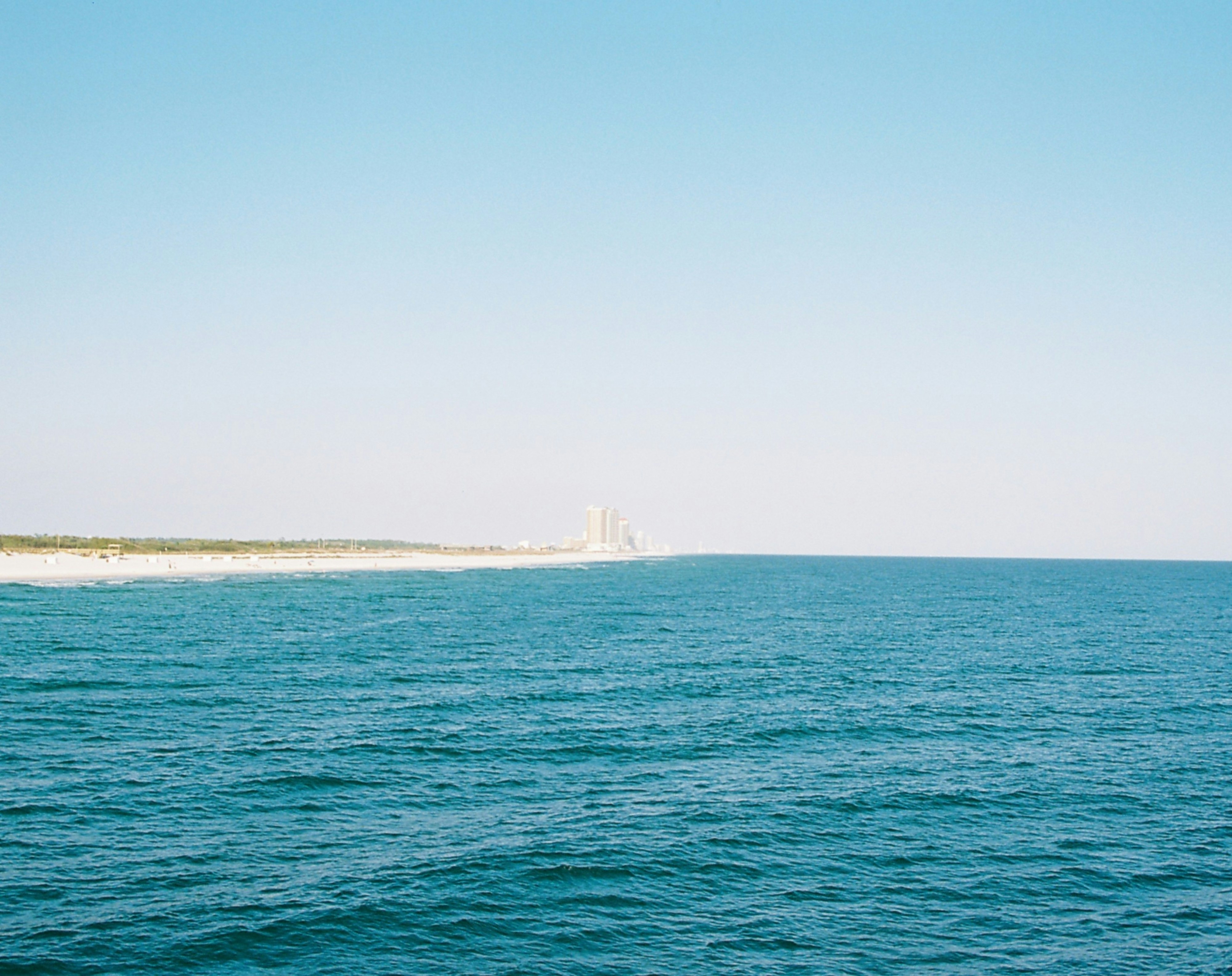 Blue ocean and sandy beach under a clear sky.