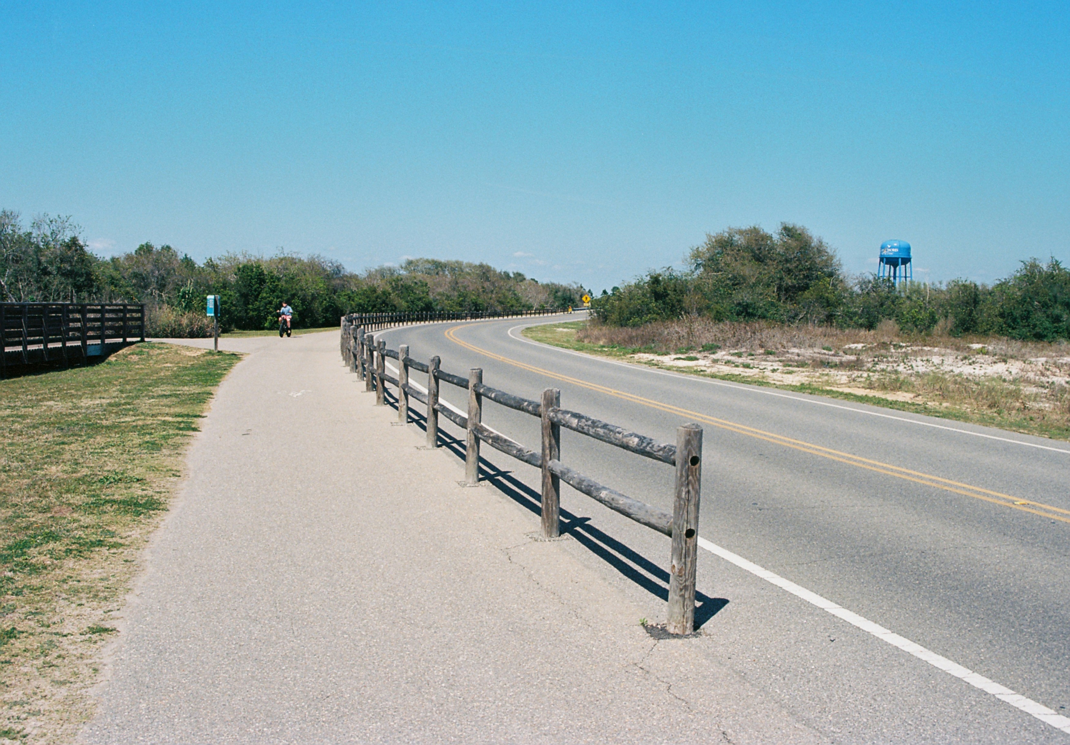 Curving road and paved path with a rustic wooden fence.