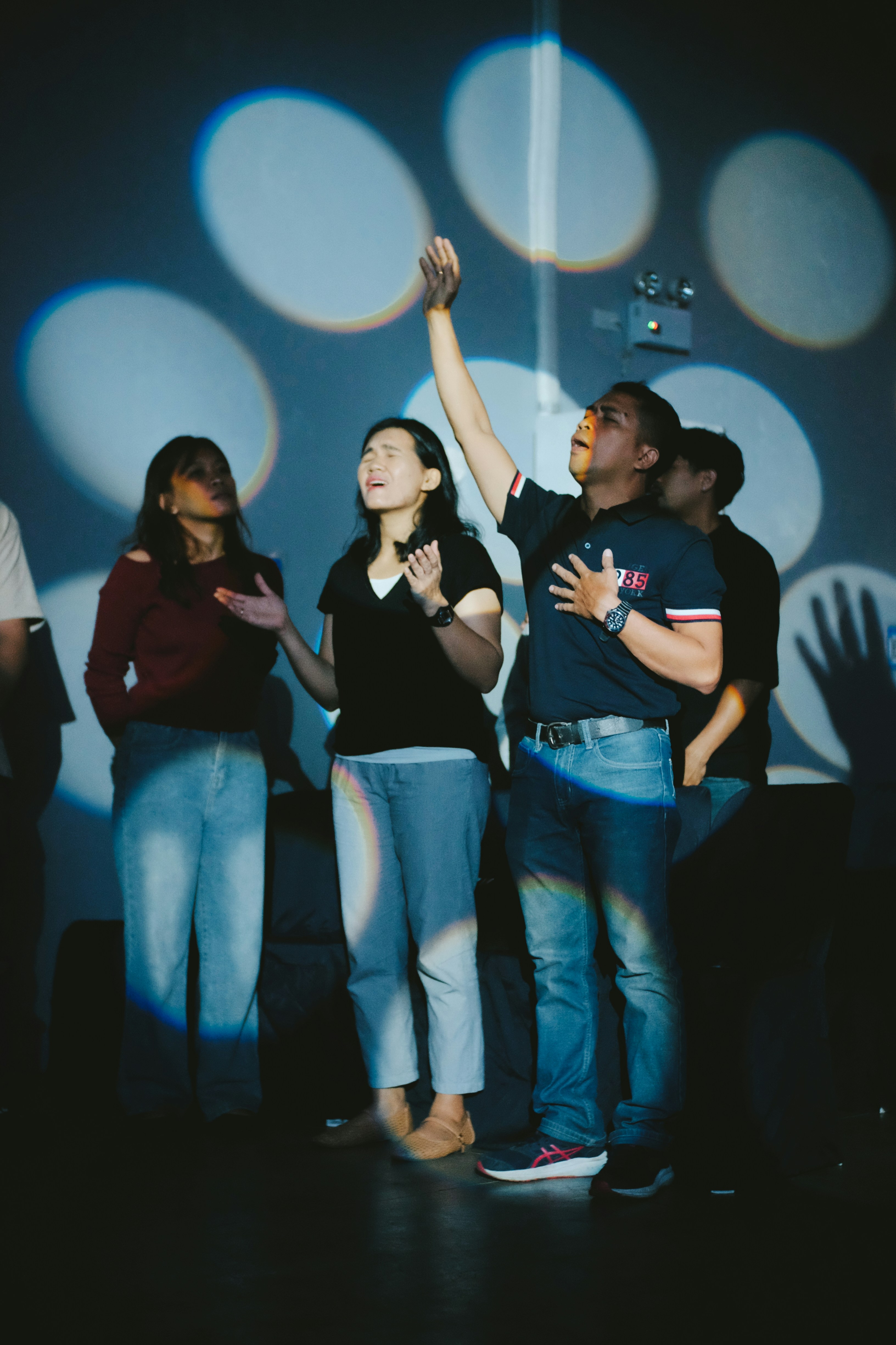 People worshiping with hands raised under spotlights.