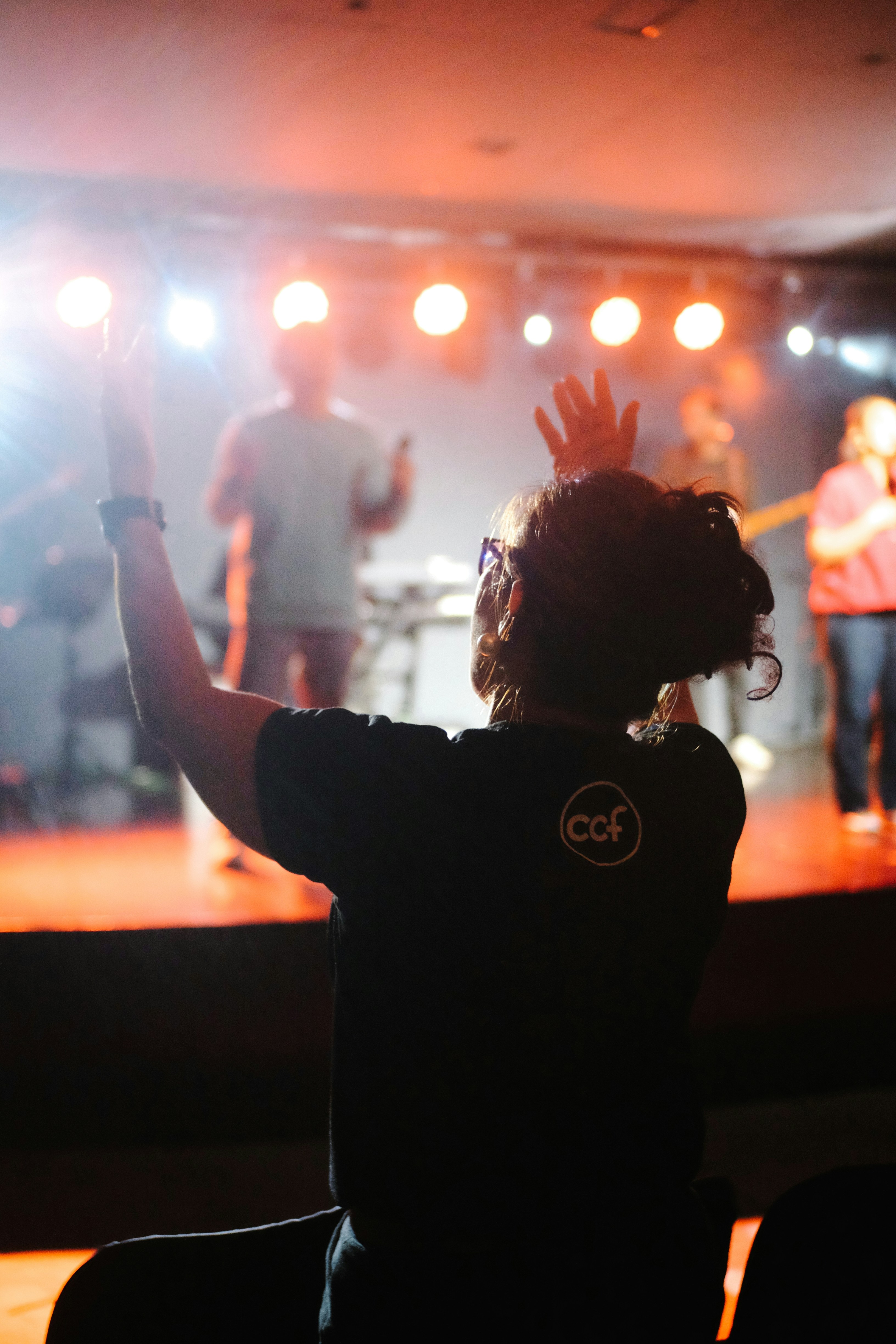 A person with raised arms watching a band on stage.