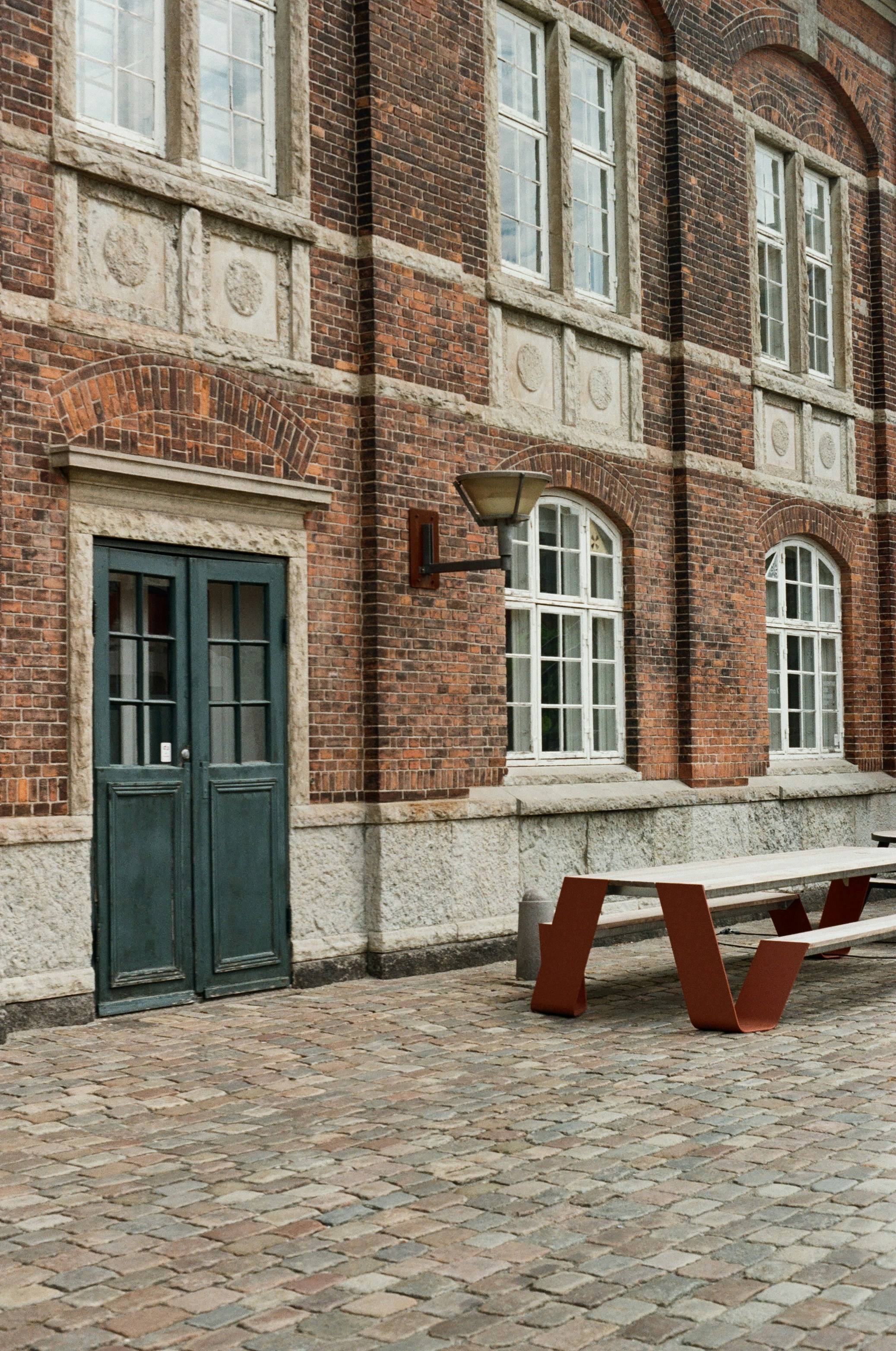 Brick building, green door, white windows, and modern picnic table.
