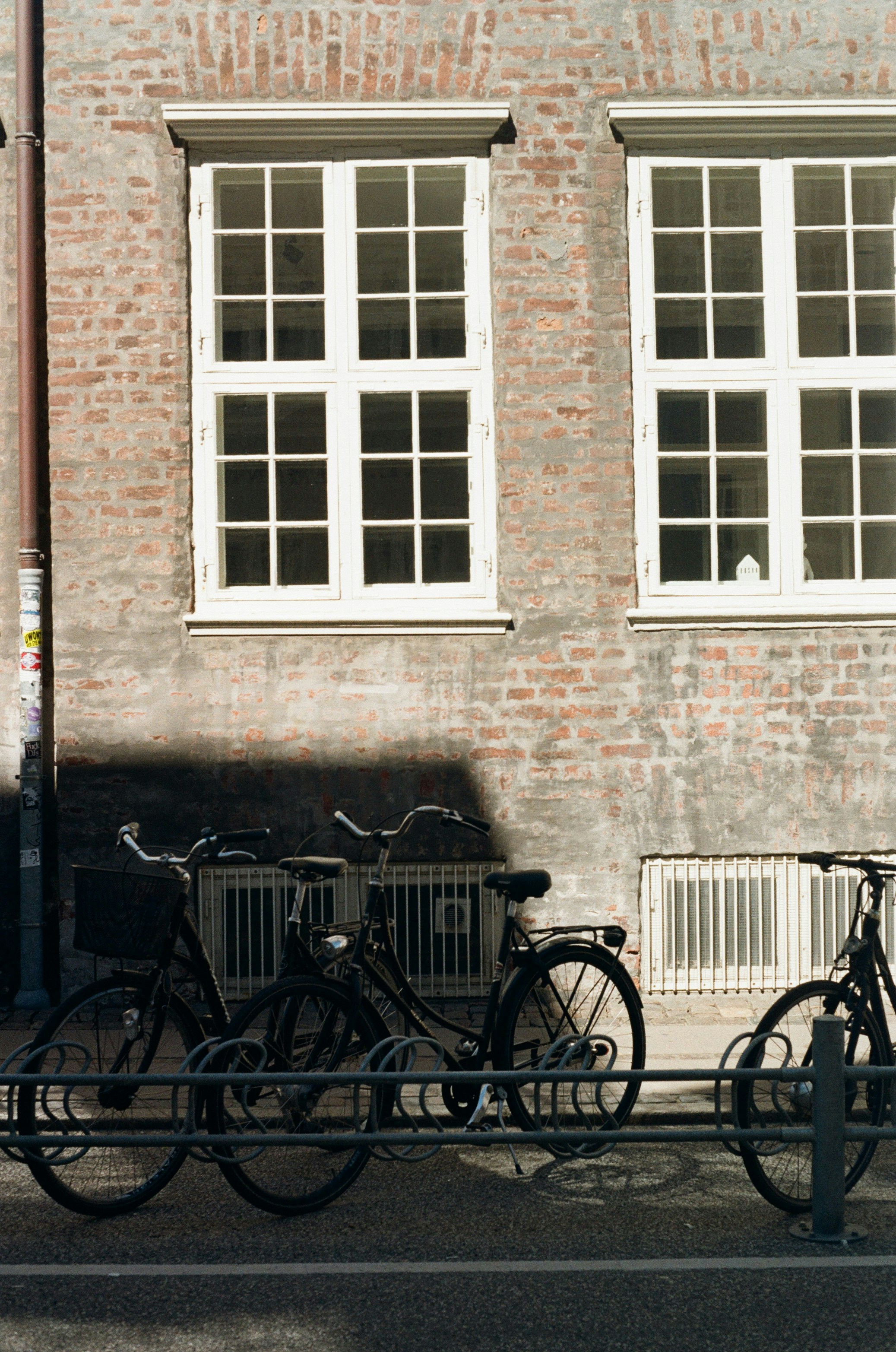 Bicycles parked against a brick wall with white windows.