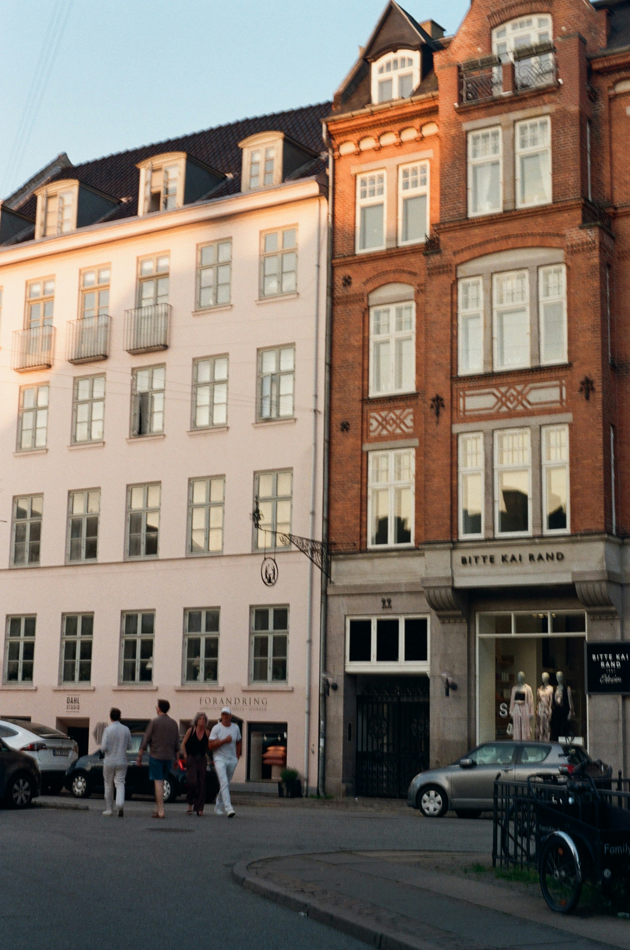 People walk past historic buildings and shops in a city.