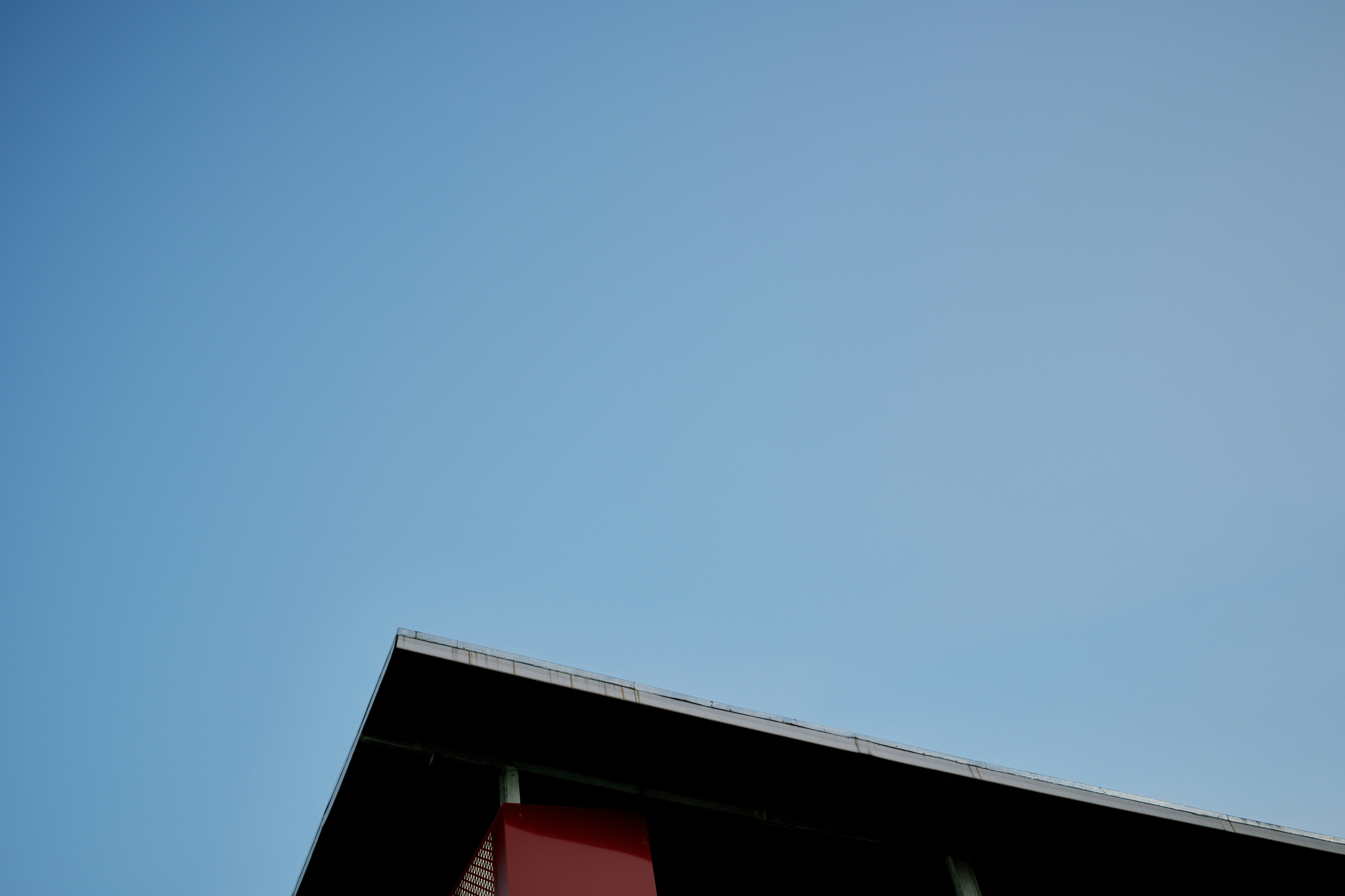 Dark building corner with red element under a blue sky.