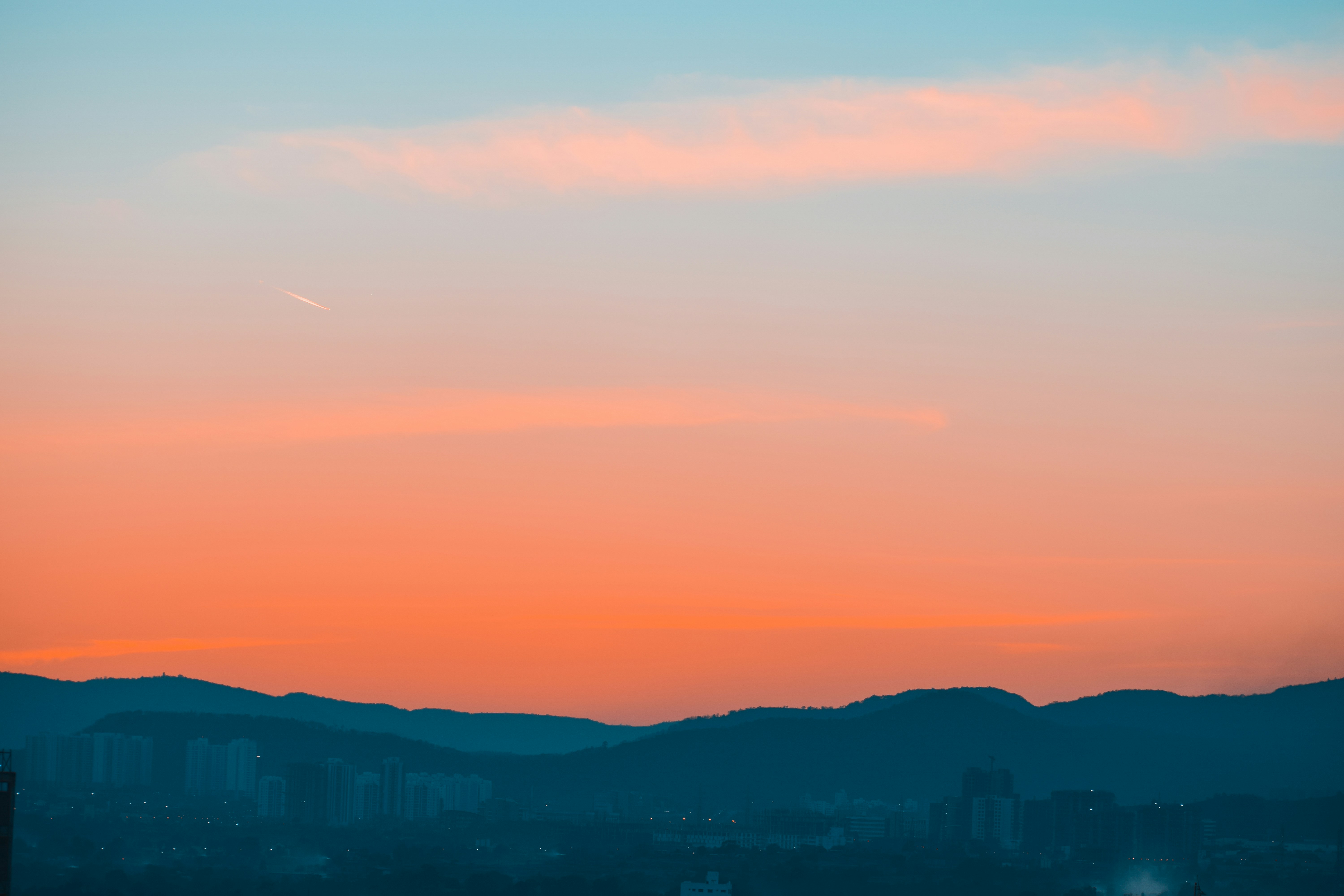 Vibrant sunset sky over dark mountains with city lights below.