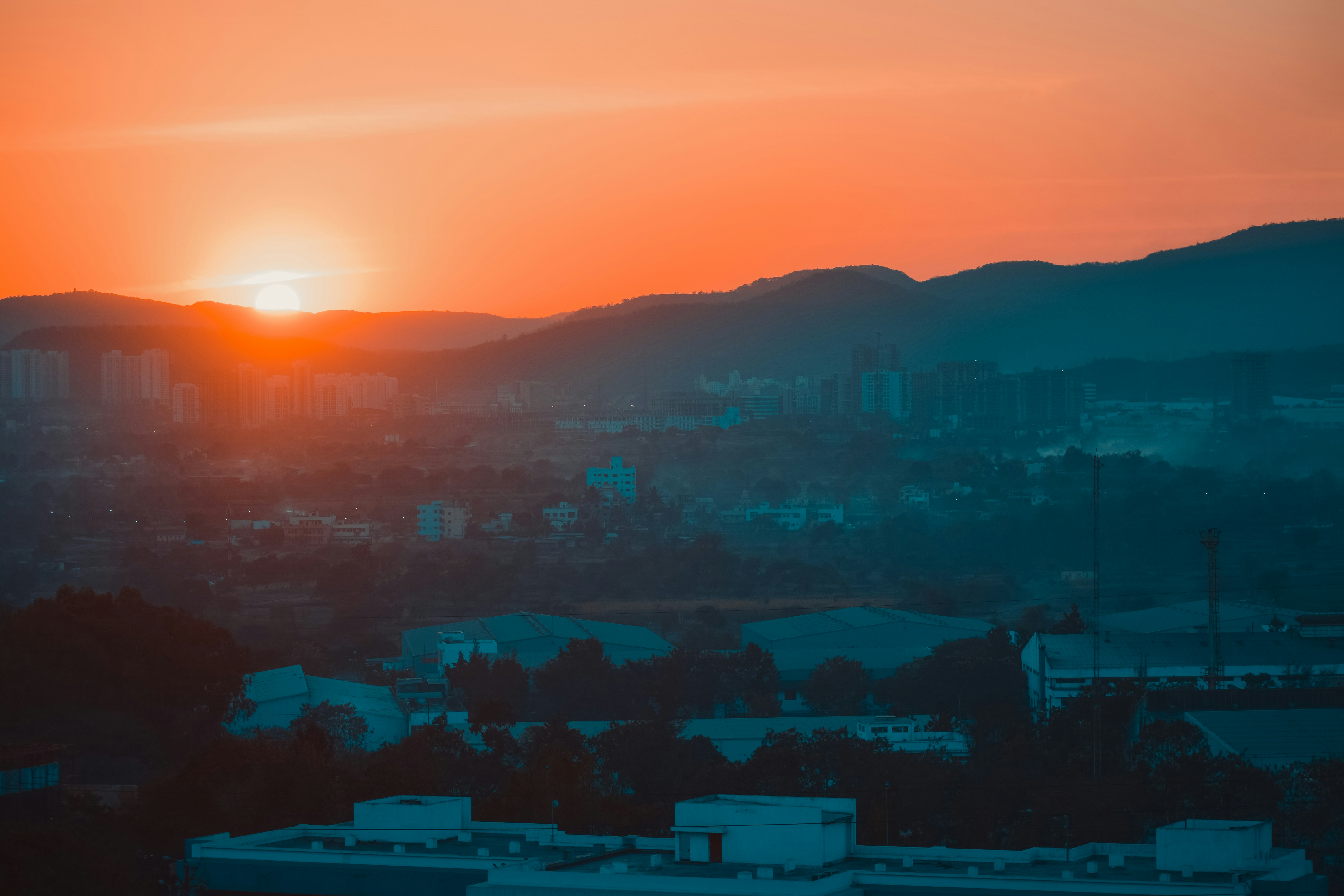 A vibrant orange sunset over a mountainous landscape and city.