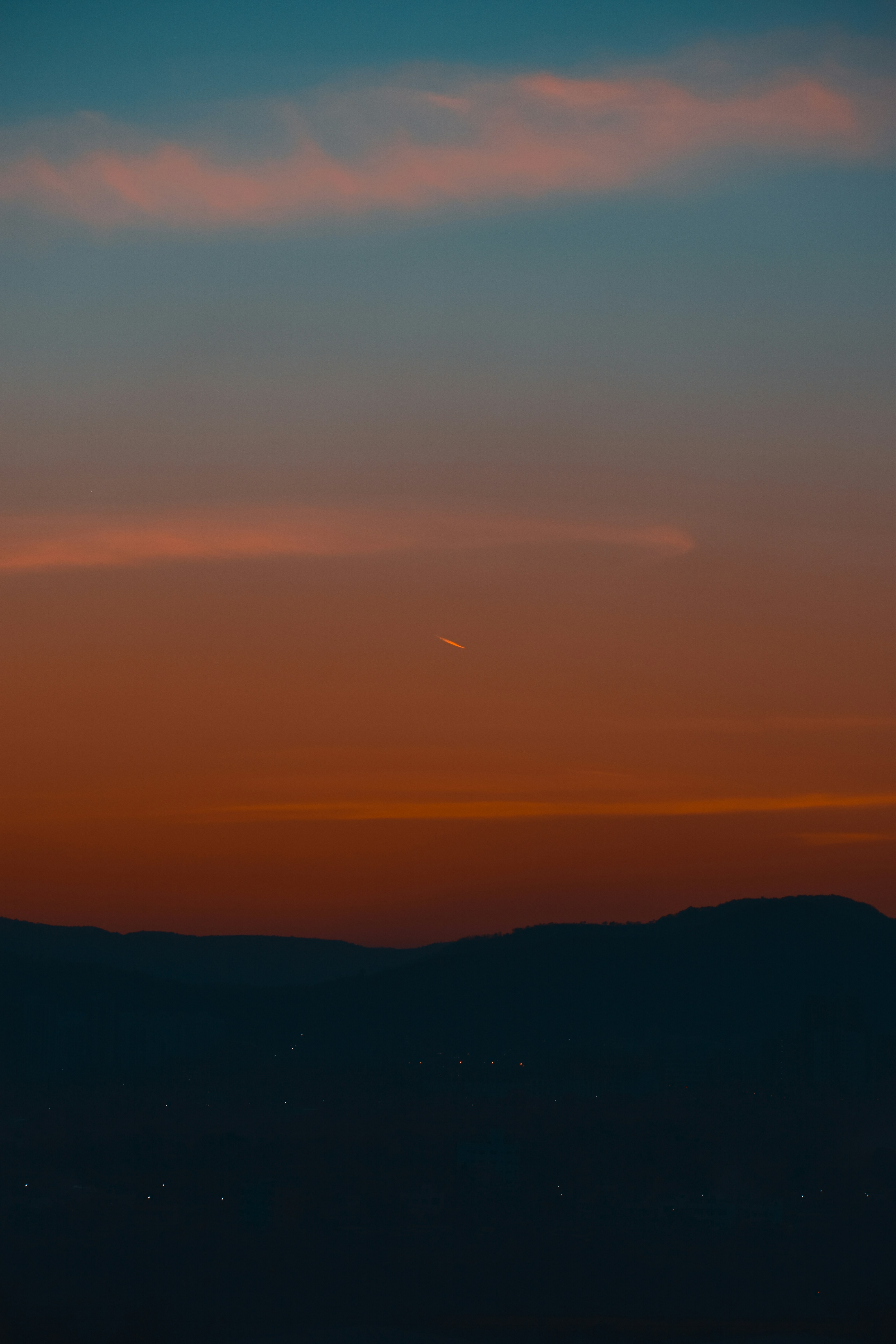 Vibrant sunset sky over dark mountains with faint city lights.