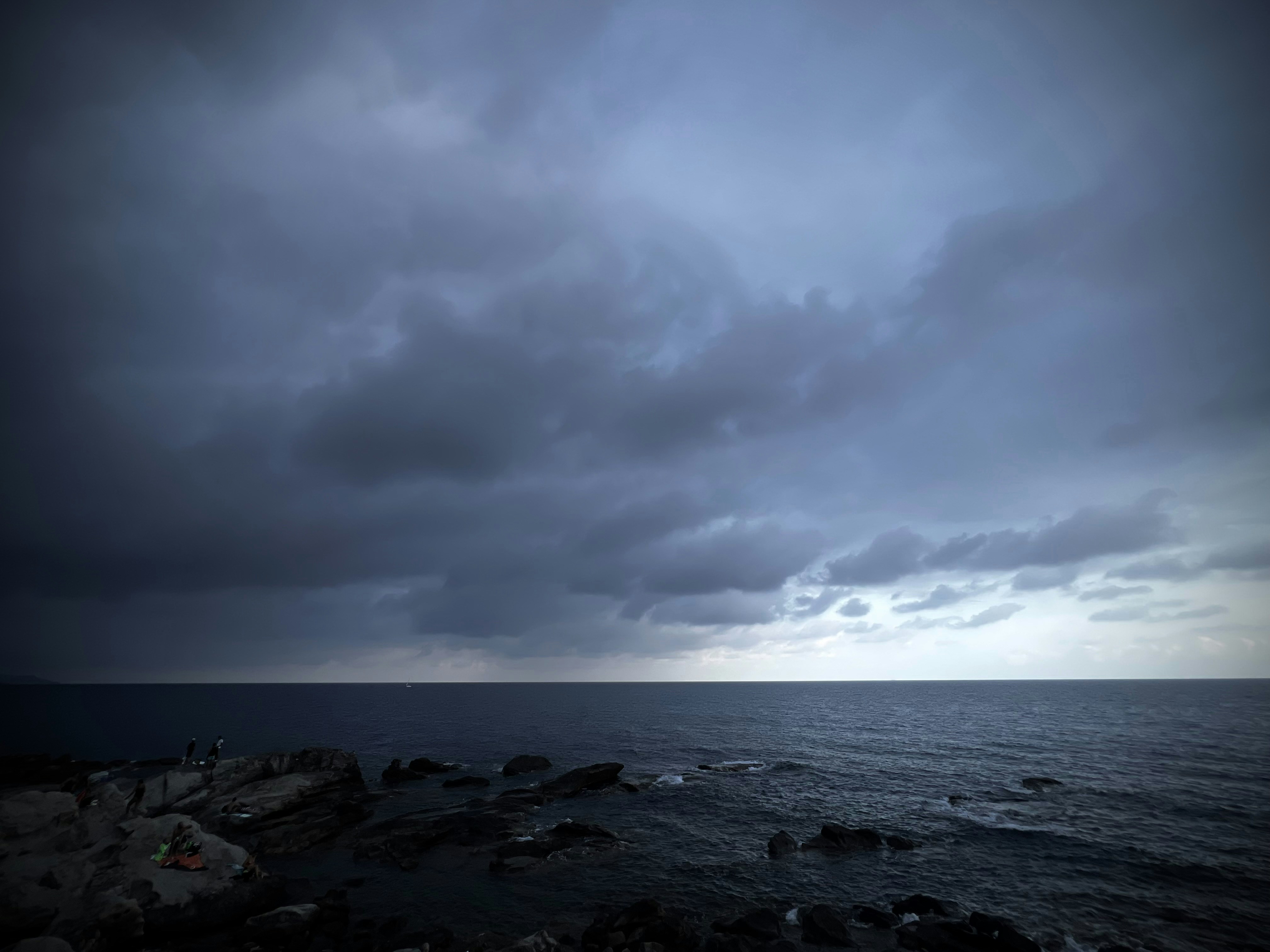 Dark storm clouds cover a moody ocean with rocky coast.